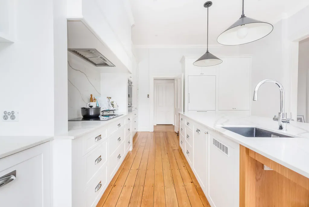 Bright modern kitchen with white cabinets, a white island with a sink, and black pendant lights, featuring hardwood floors.