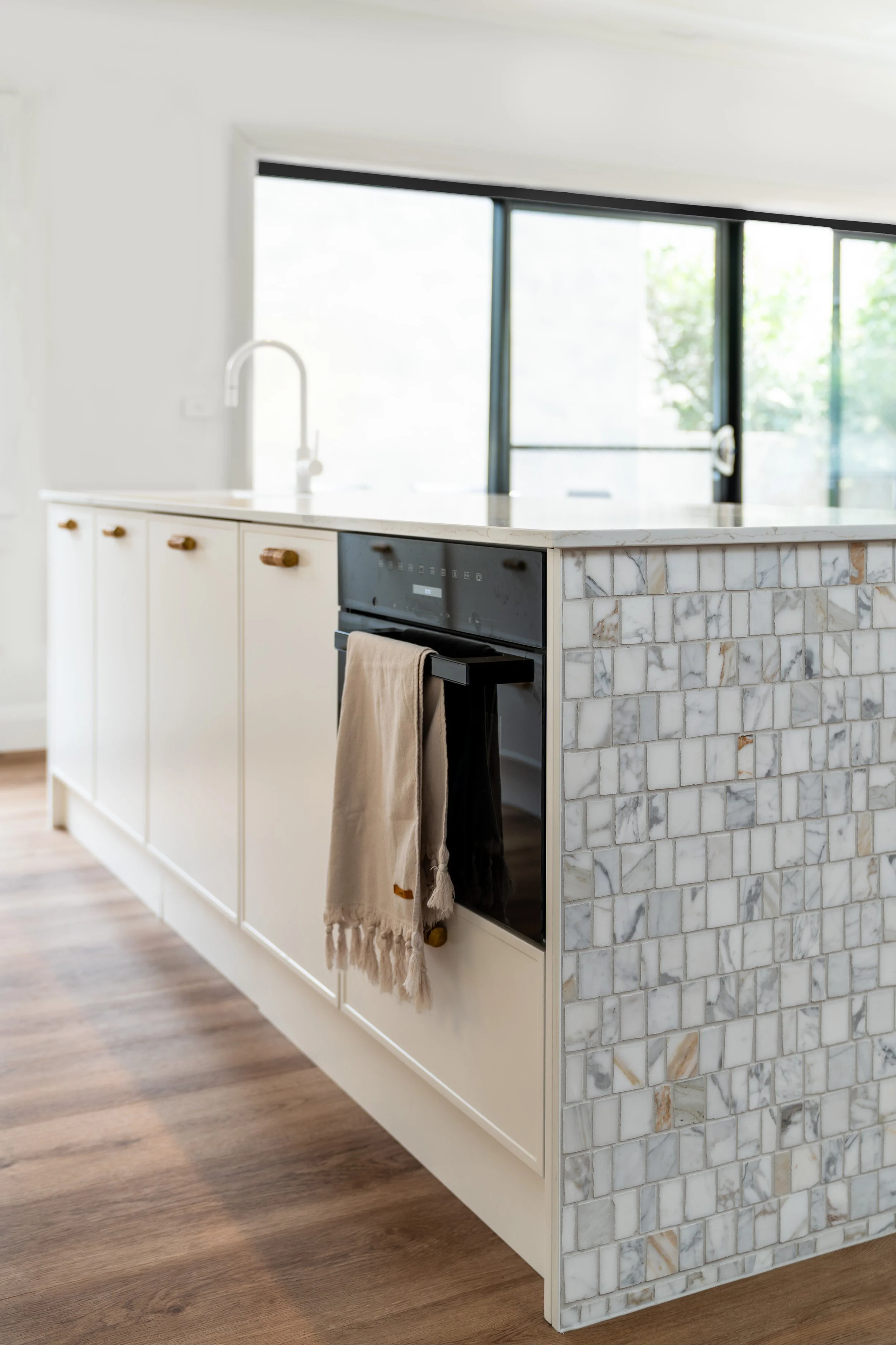 A kitchen island with a marble countertop and a mosaic tile base, with a beige and black towel hanging from the oven handle.