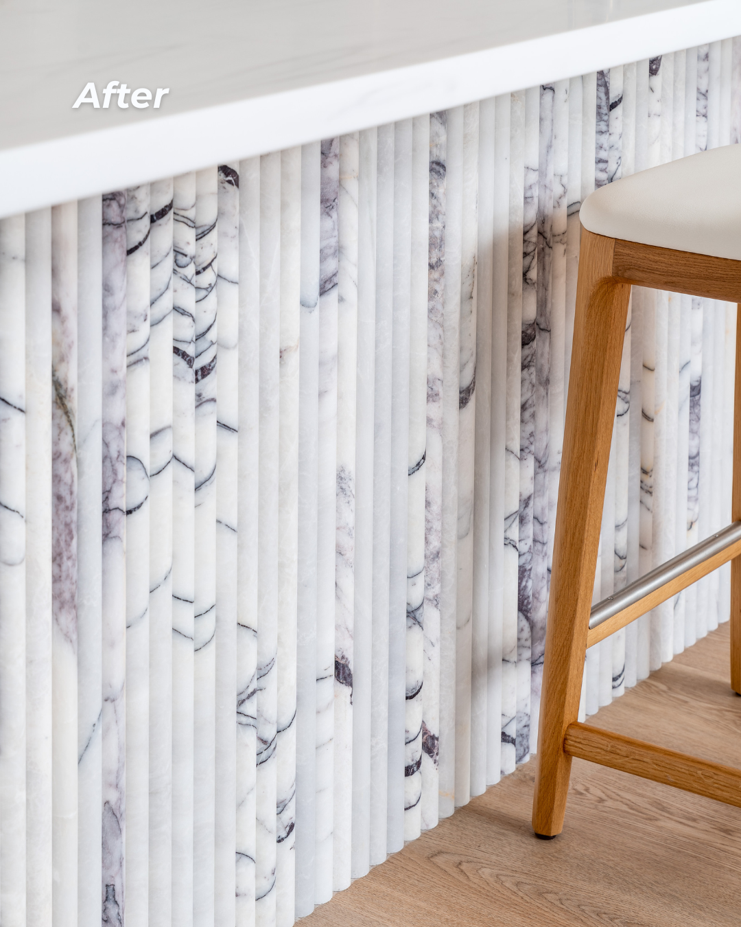 Marble-textured kitchen island with vertical marble panels and a light wooden chair with a cushioned seat nearby.