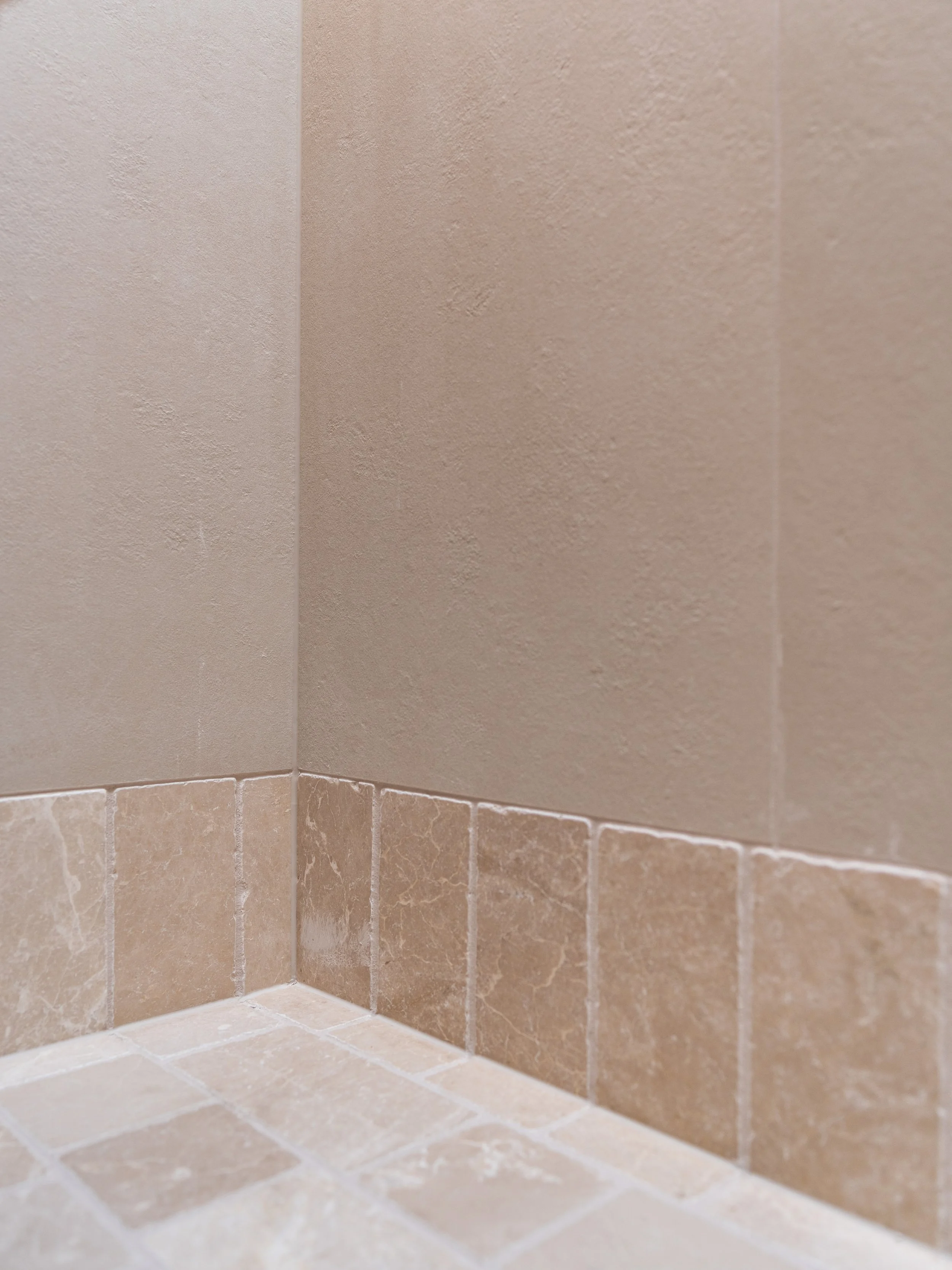 Close-up of tiled bathroom wall with beige and light brown tiles, showing the corner of the shower or bathtub area.