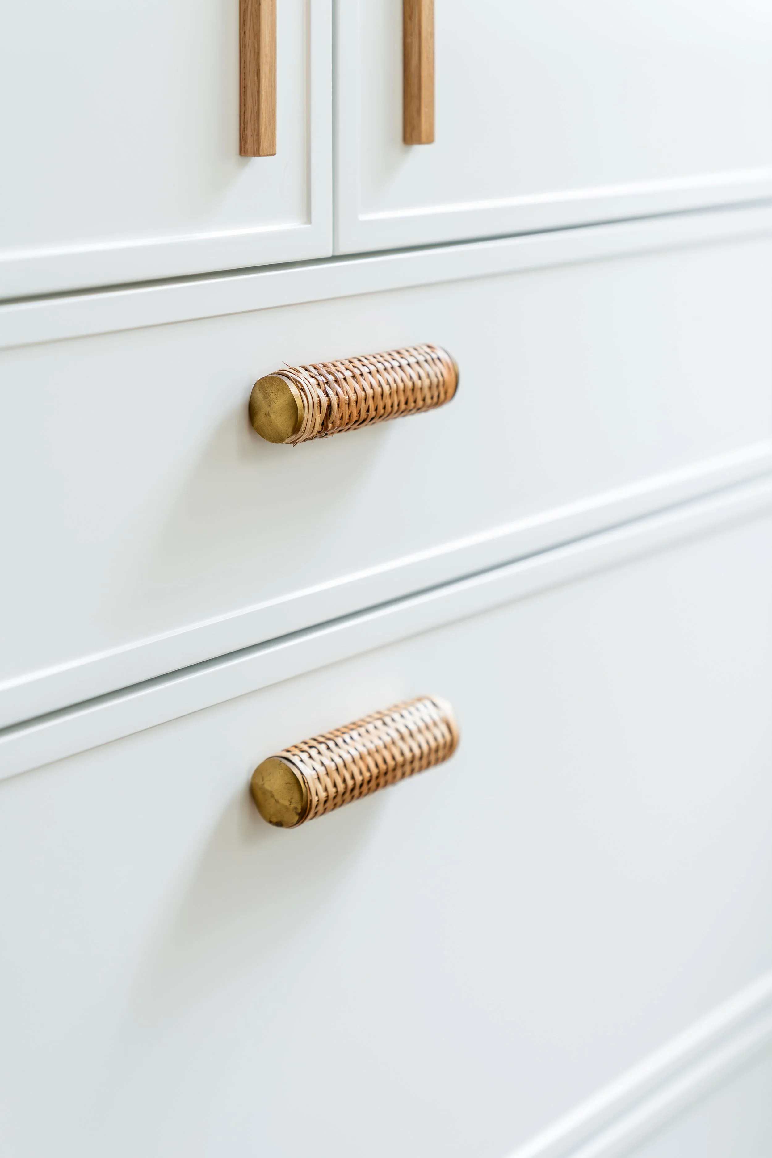 Close-up of a white cabinet with wooden handles and woven wicker drawer pulls.