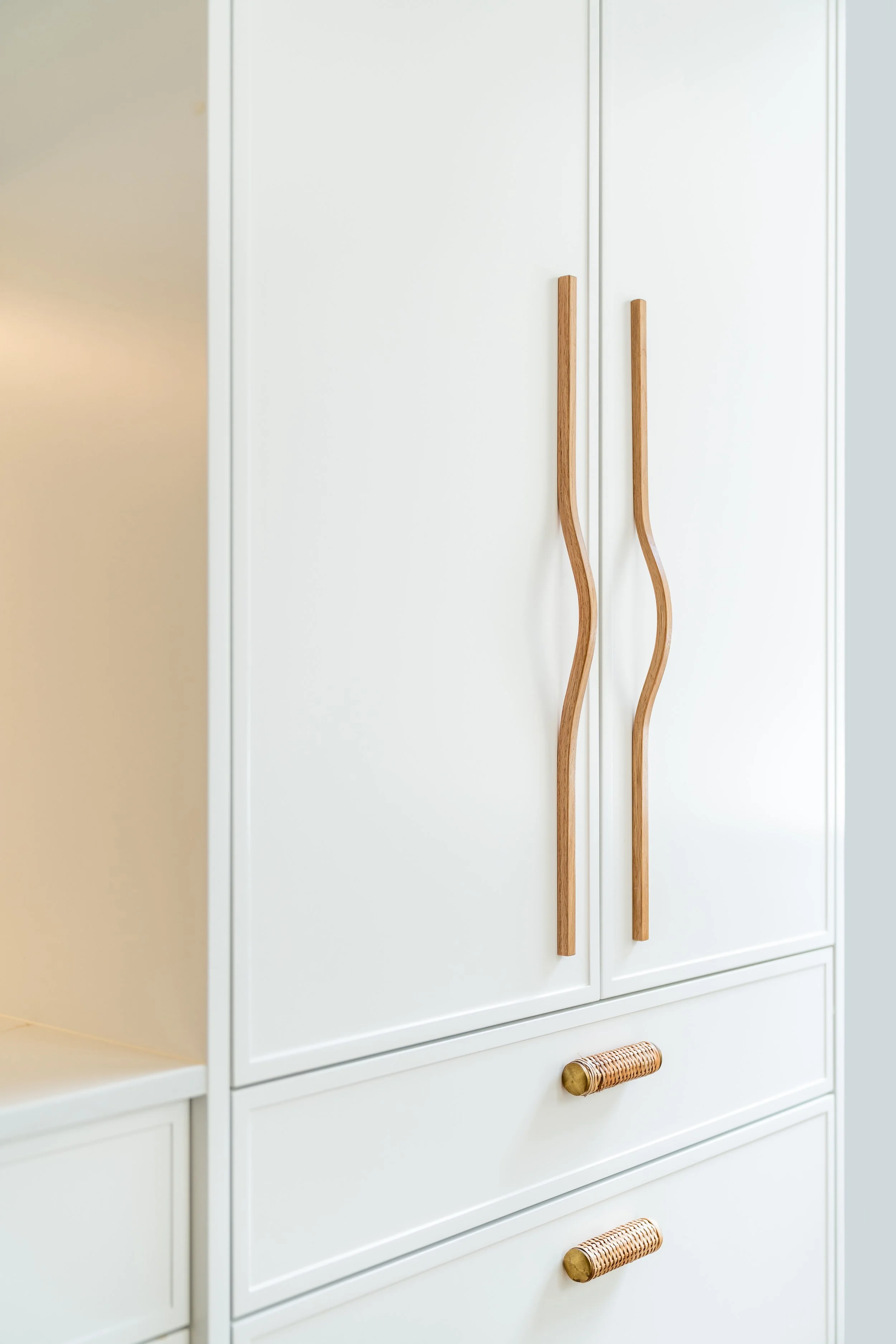 White built-in cabinet with wooden handles and rattan-covered knobs in a minimalist style.