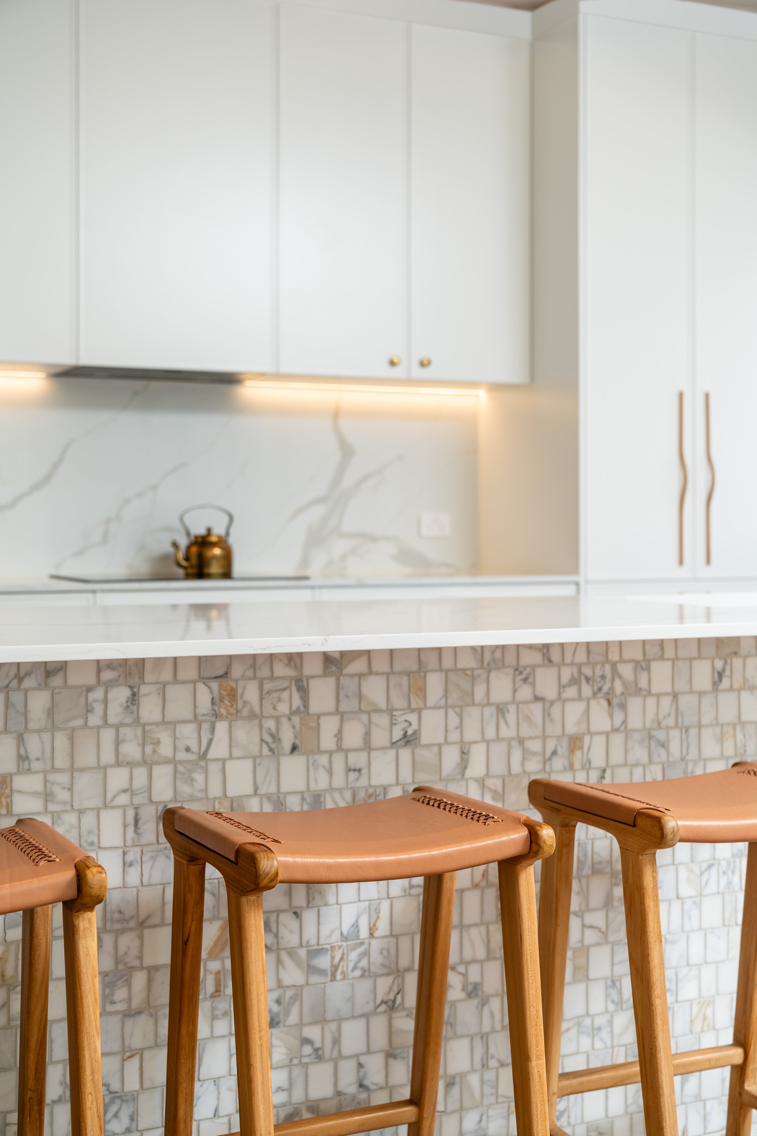 A modern kitchen with white cabinets, a marble backsplash, a marble countertop, and wood bar stools.