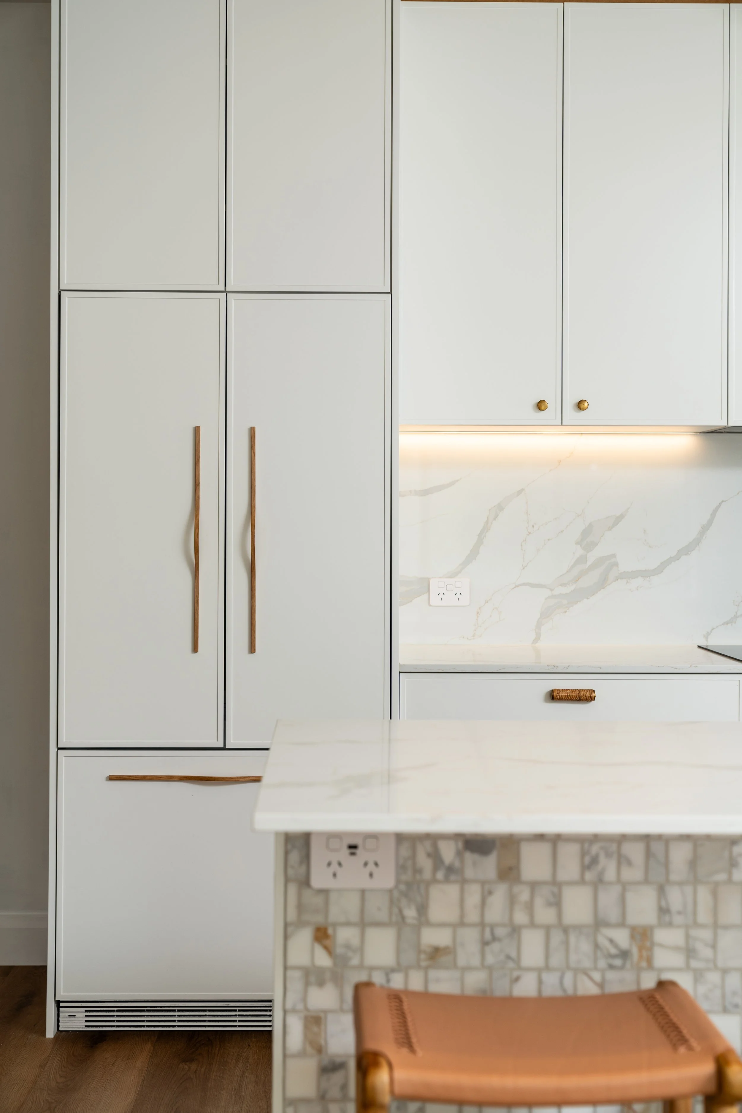 Modern kitchen with beige cabinetry, marble backsplash, and a small brown leather chair at the table.