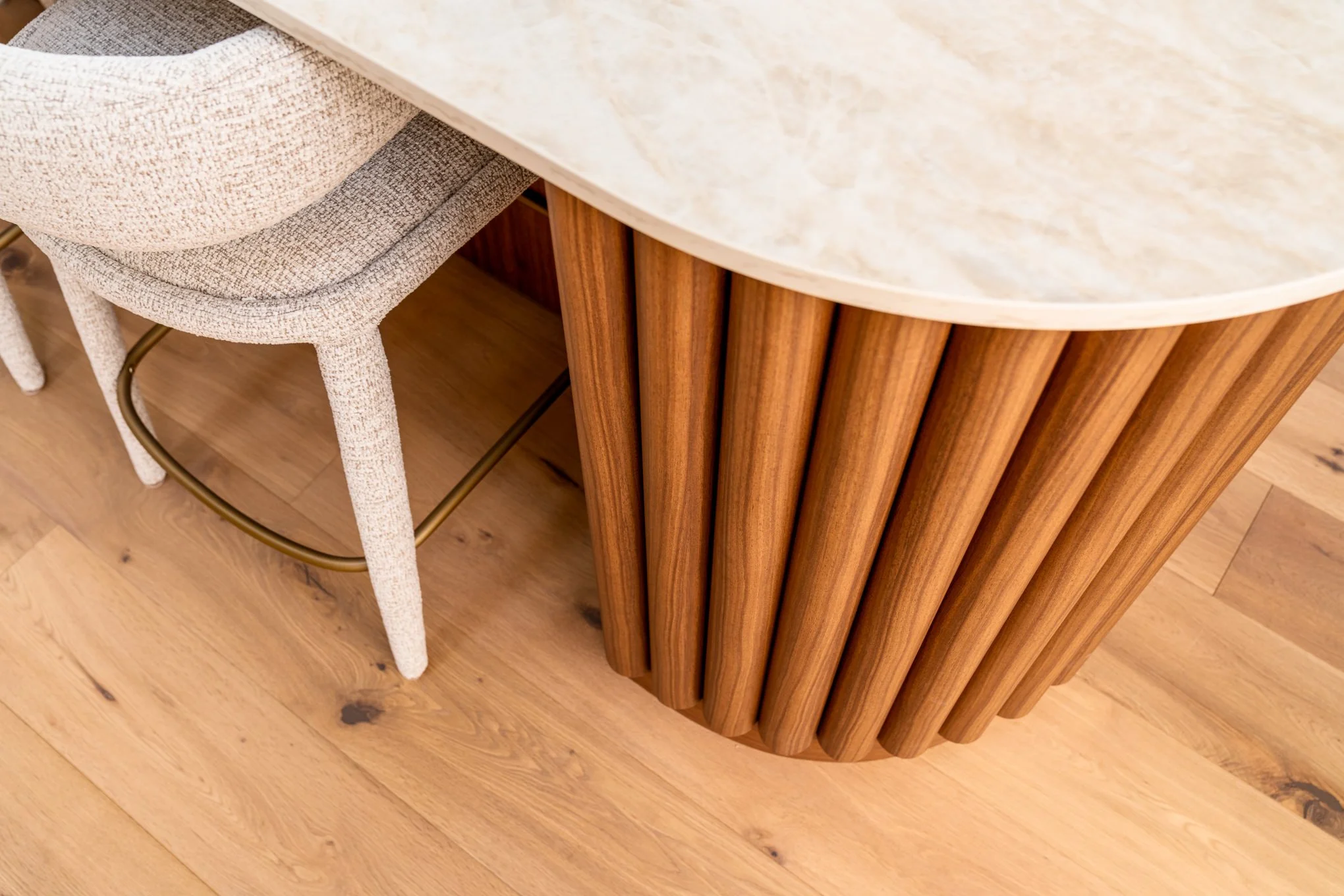 Close-up of a beige upholstered chair next to a wooden table with a rounded edge, on a hardwood floor.