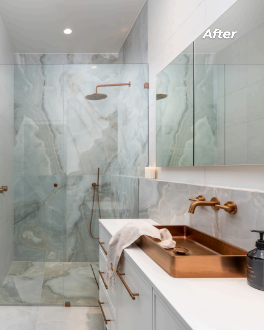 Modern bathroom with marble walls, walk-in shower with copper fixtures, white vanity with copper sink, large mirror, and neutral decor.