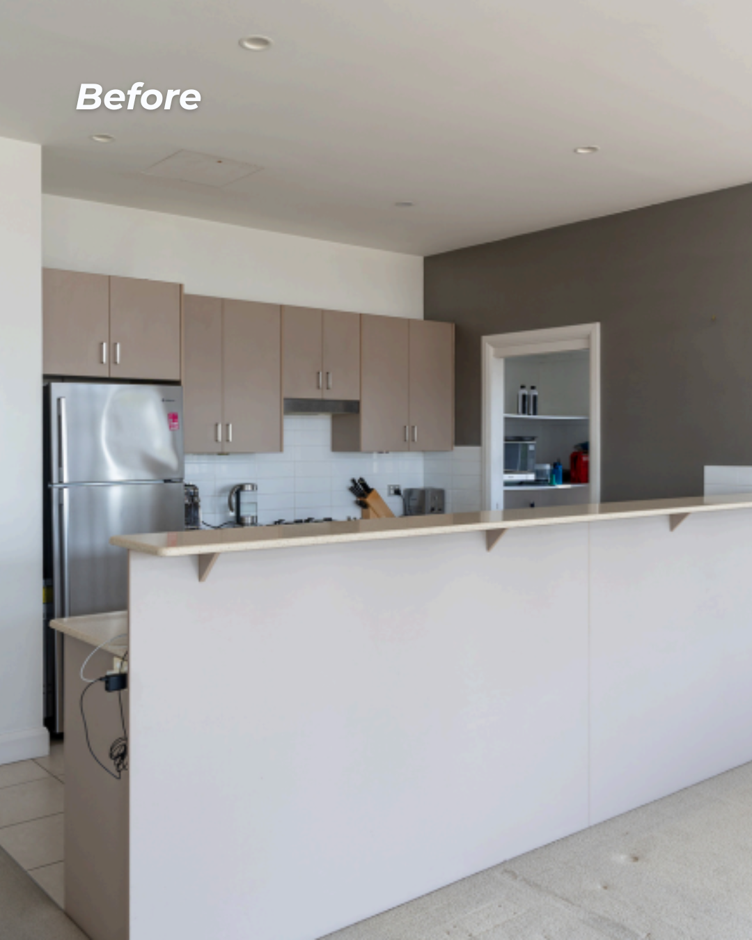 Empty kitchen with beige cabinets, a stainless steel refrigerator, white subway tile backsplash, and a breakfast bar.