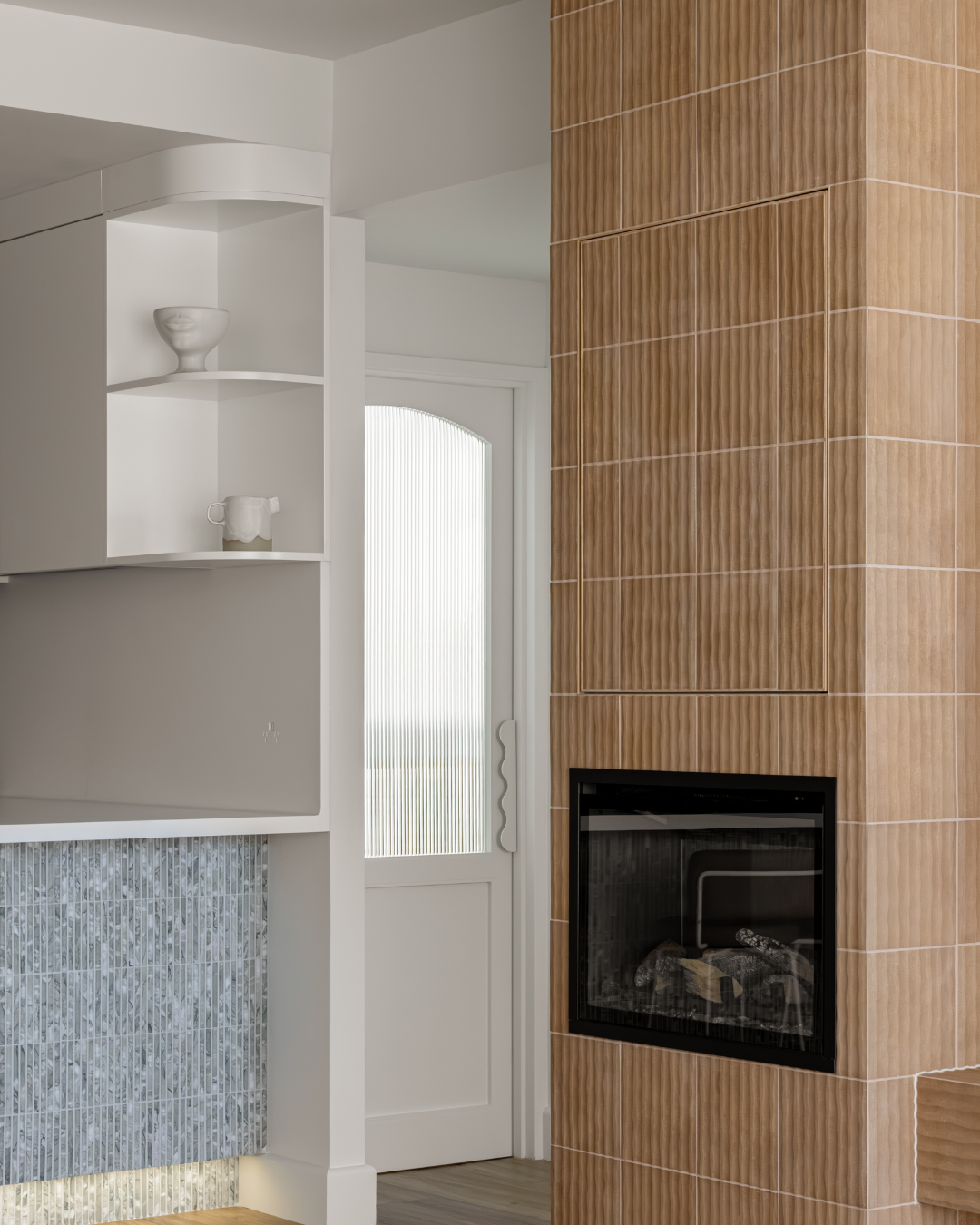 Interior of a modern home with a tiled fireplace, wooden wall tiles around the fireplace, white shelves with ceramic decorative items, and a door with frosted glass panel.