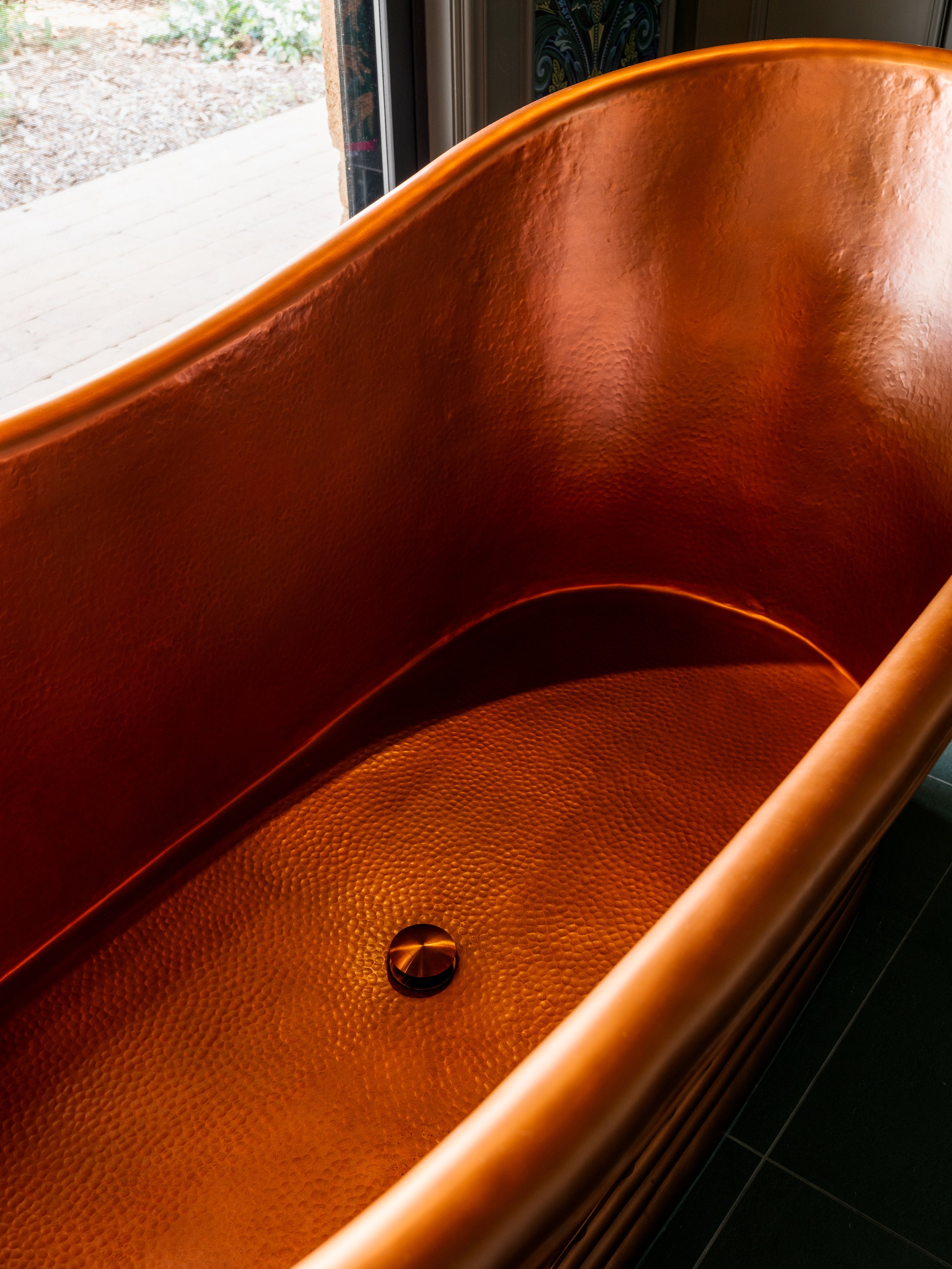 Close-up of an orange, textured, curved interior surface of a tub or large container, with a small round metallic knob at the bottom.