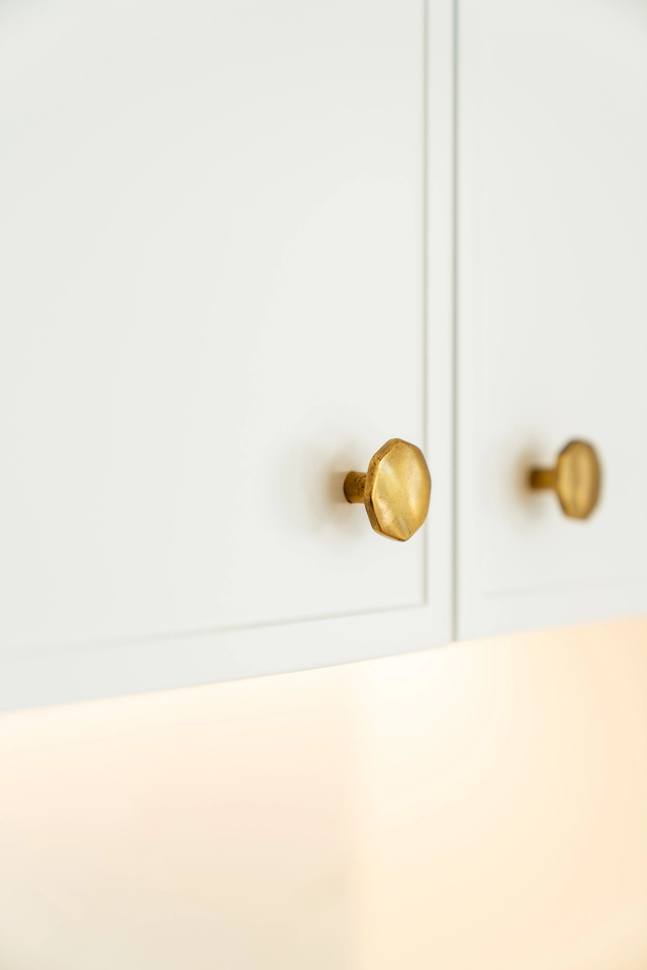 A white cabinet with a vertical silver handle and two smaller gold knobs on the door.