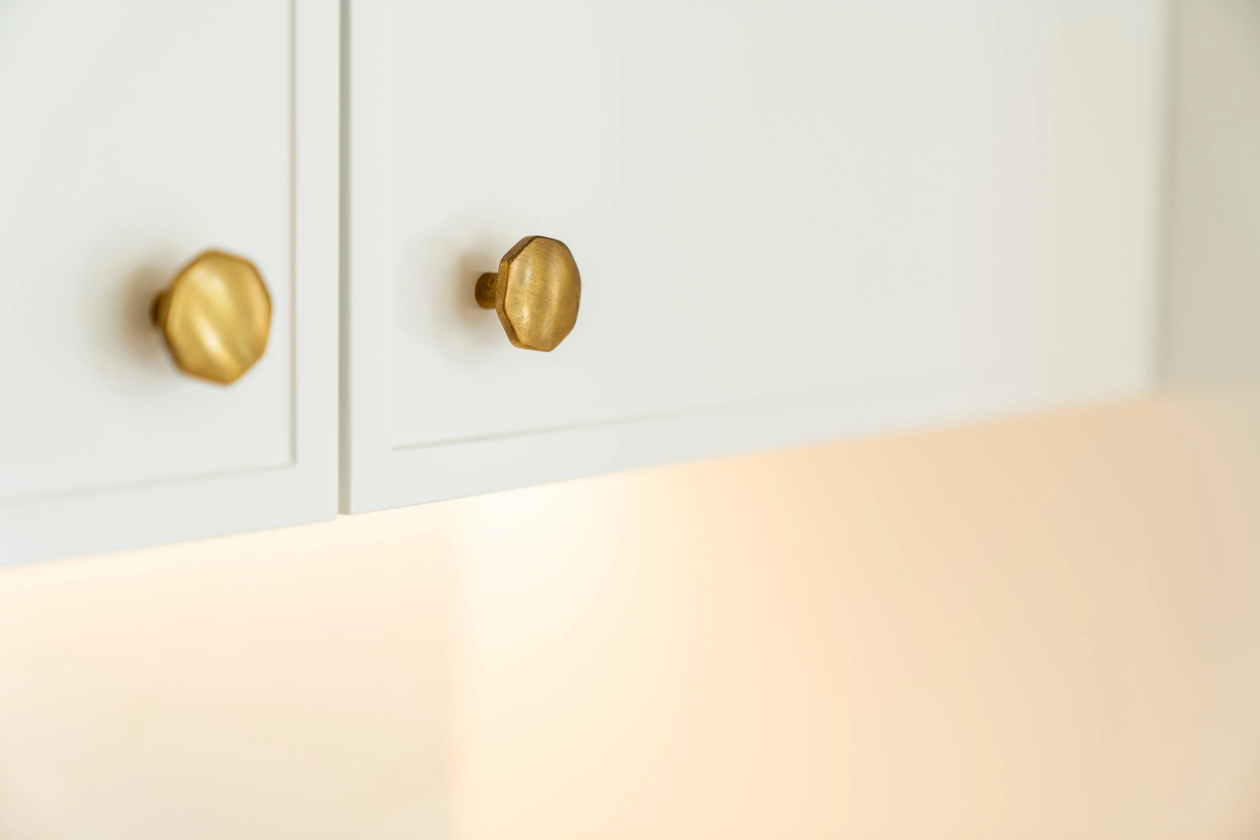 Close-up of a white cabinet with two brass knobs, with a minimalistic and modern design.