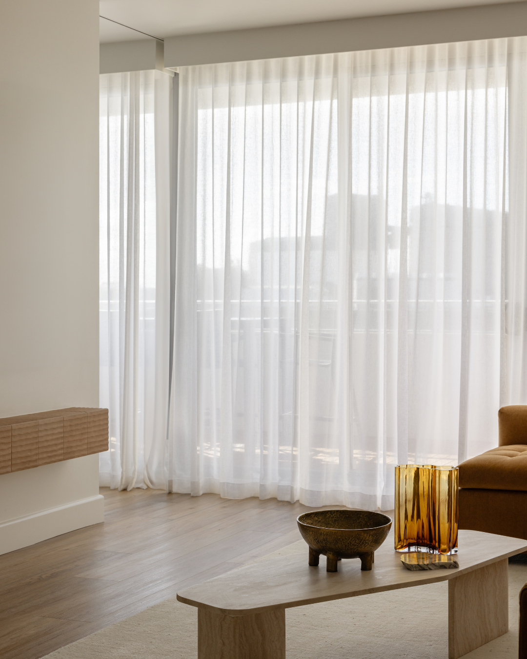 Living room with sheer white curtains, a beige chair, and decorative accessories on a wooden table.