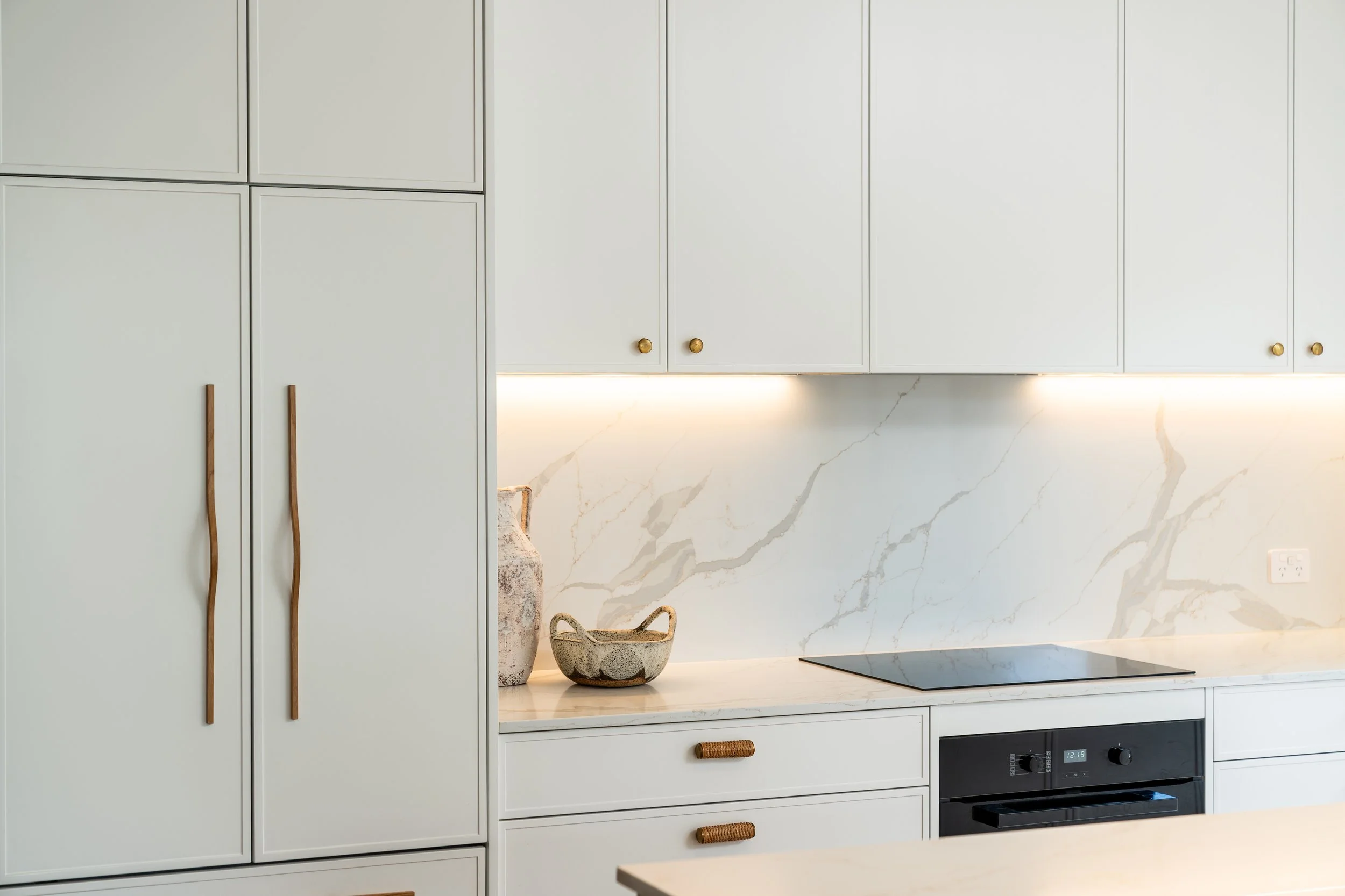 White kitchen cabinets with gold knobs, marble backsplash, a beige textured bowl, and a smaller decorative bowl on the countertop.