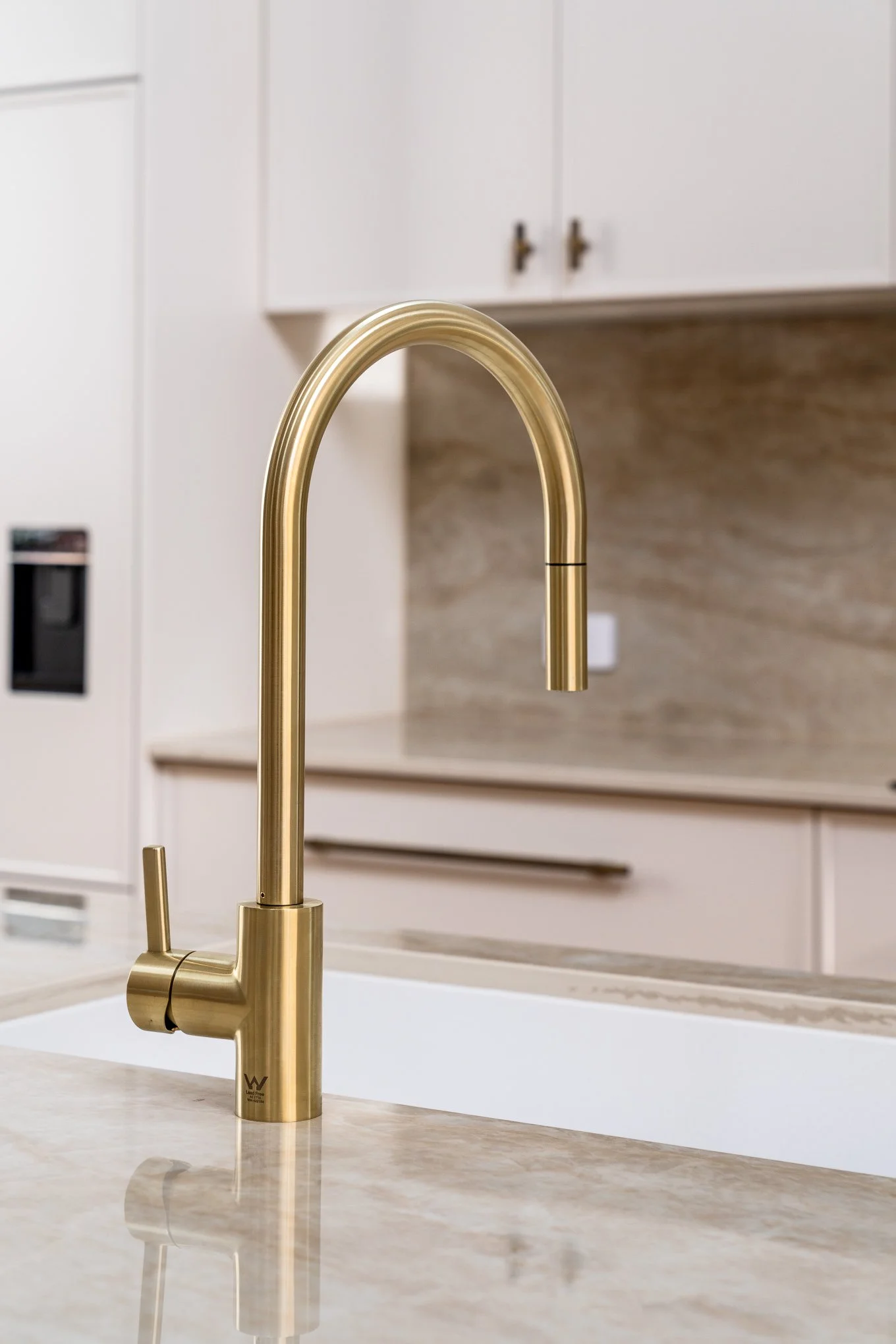Close-up of a gold-colored kitchen faucet on a cream marble countertop with white cabinets in the background.