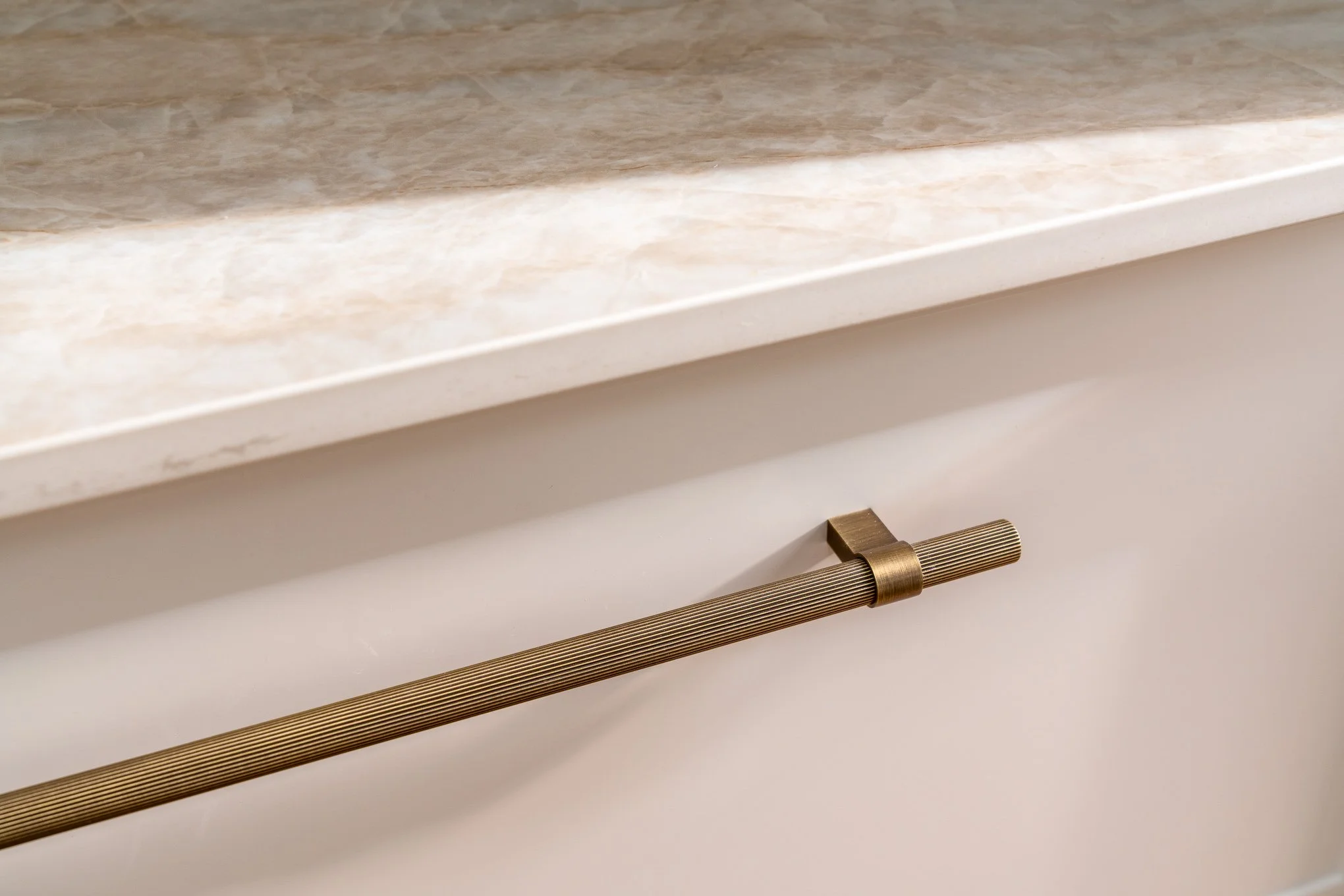 Close-up of a cabinet drawer with a gold-colored, textured, horizontal handle beneath a marble countertop.