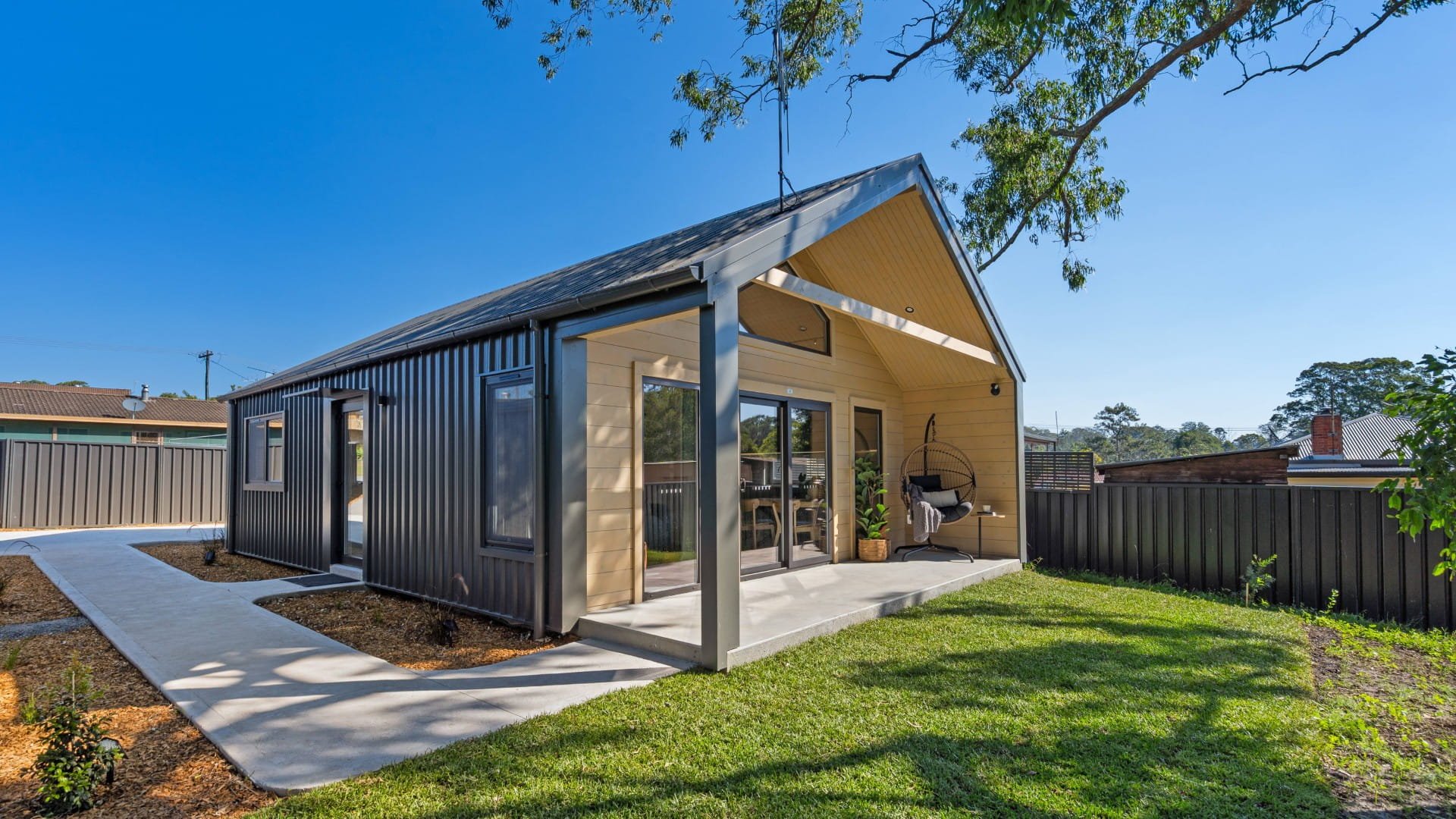 Modern house with a Yard and a covered patio, black and cream exterior, and large windows, under a clear blue sky.