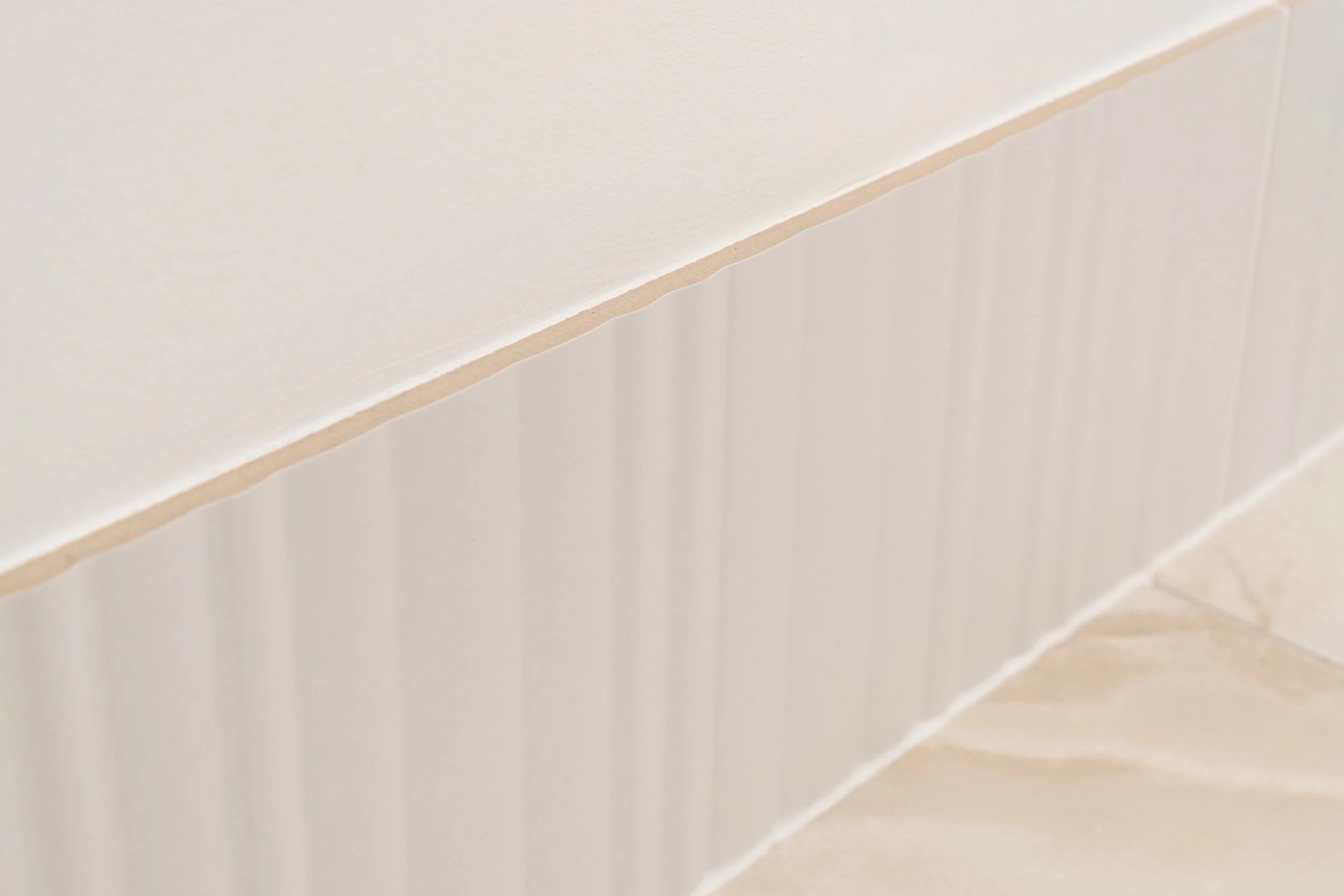 Close-up of a beige and white tiled wall with seam lines.