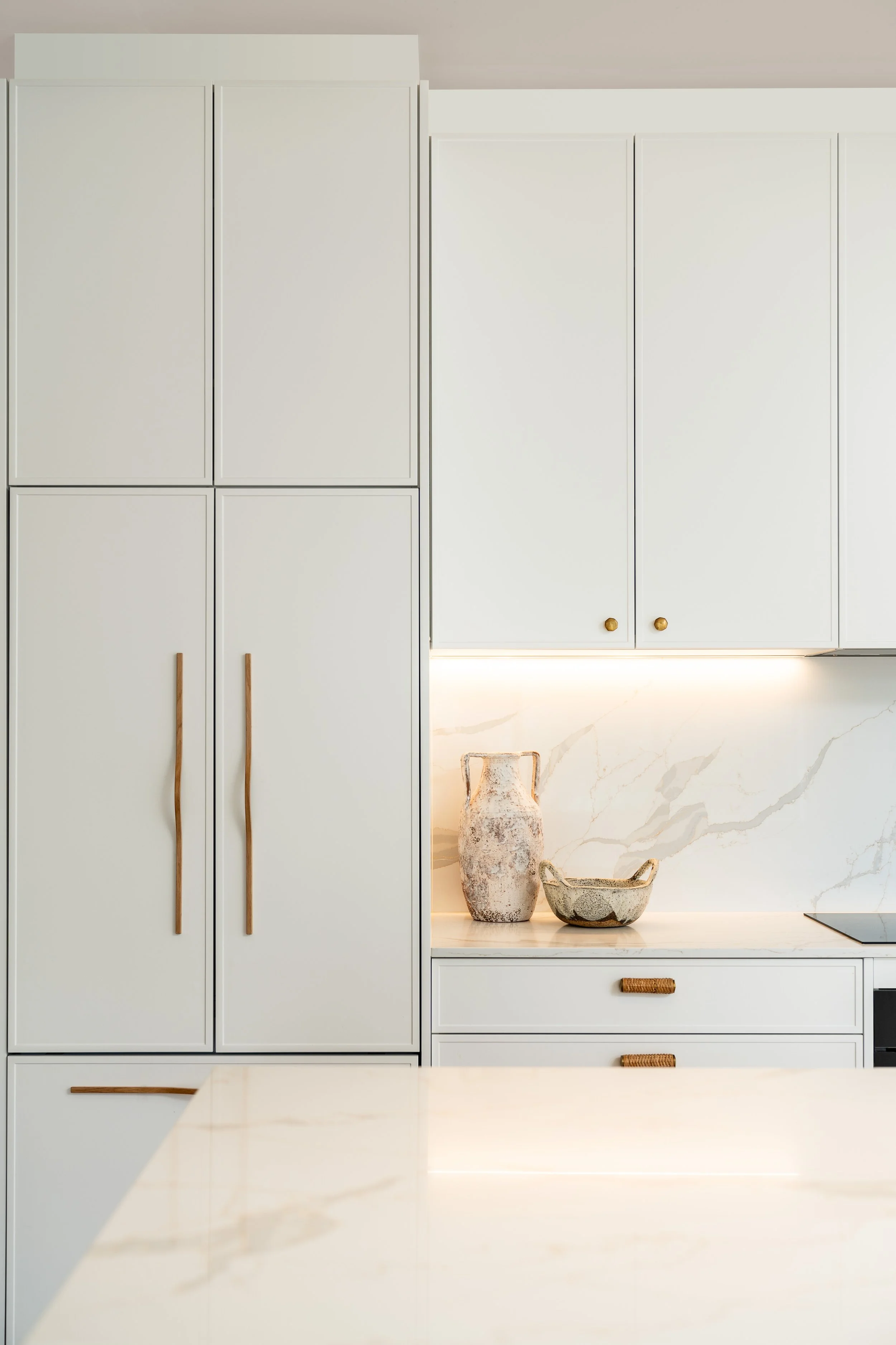 Modern white kitchen with cabinets, marble countertops, and decorative vases.