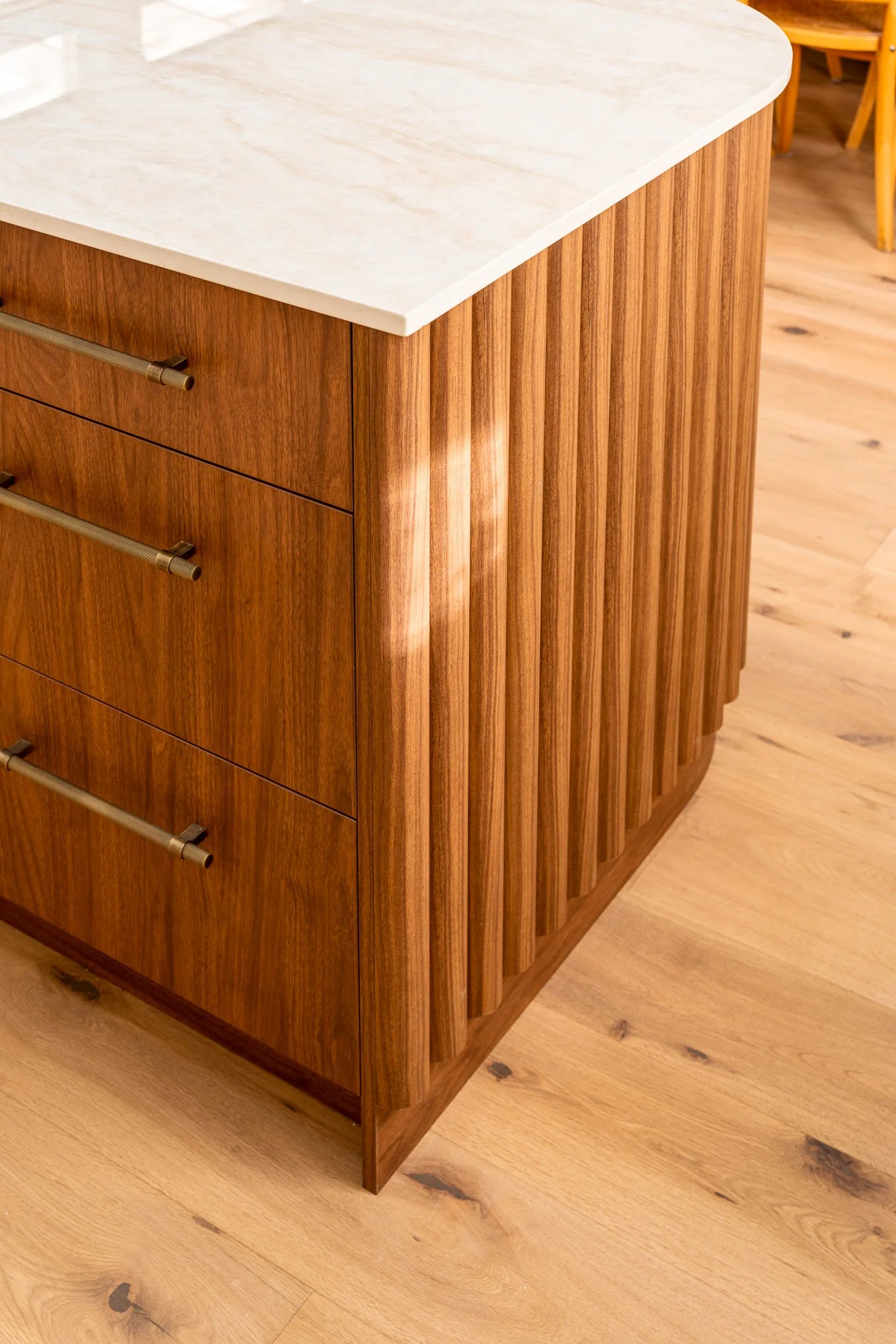 Close-up of a wooden cabinet with vertical slats and three drawers, topped with a white marble countertop, on a wooden floor.