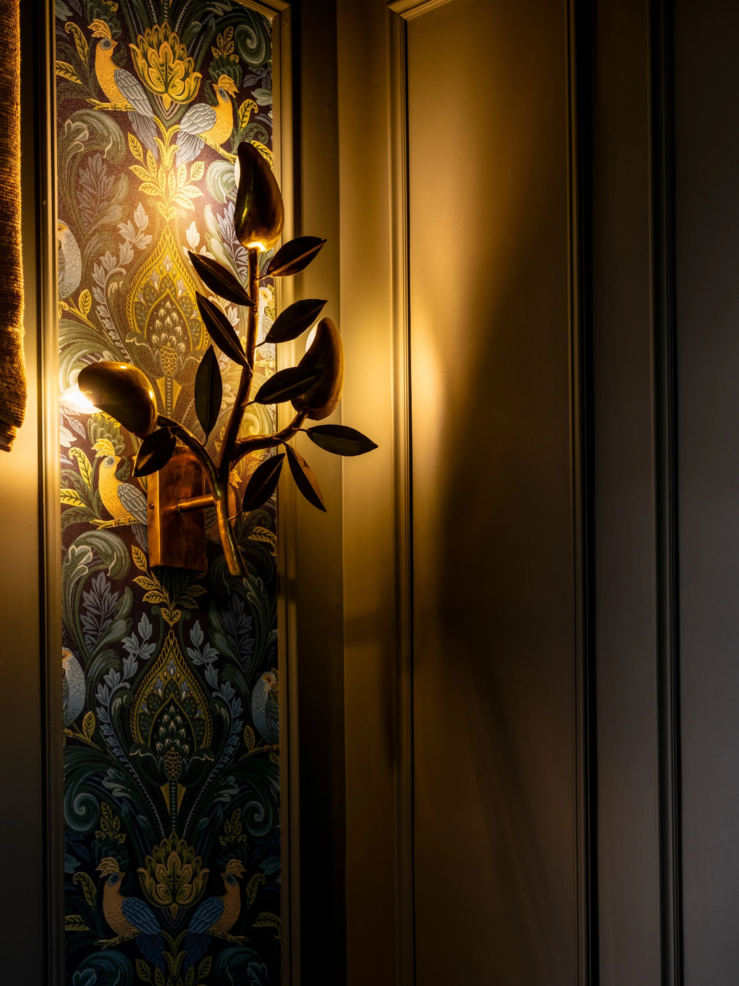 Decorative panel with peacocks and ornate patterns, door handle, and framed artwork or wallpaper on the wall with warm lighting.