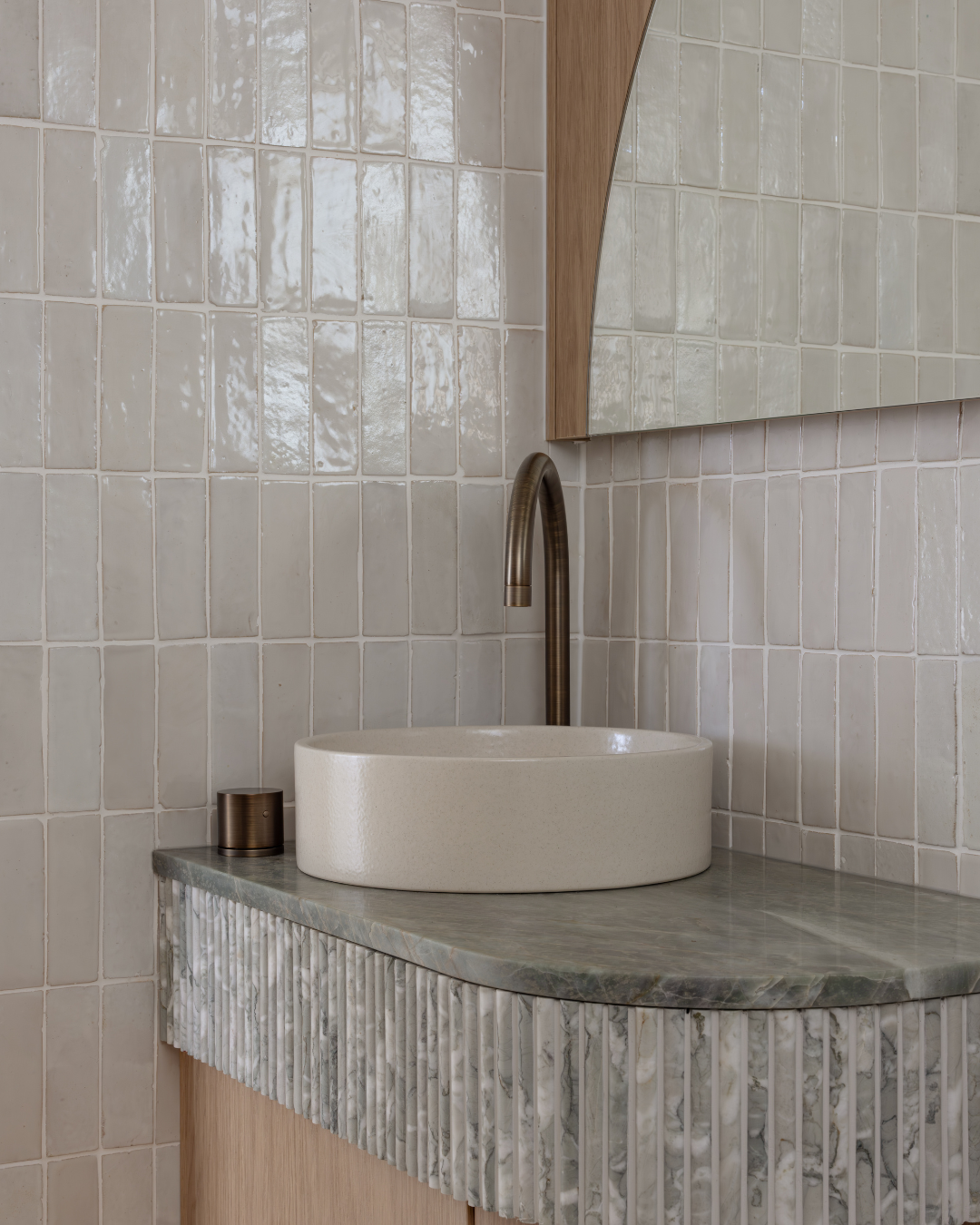 Bathroom sink with a beige countertop, a vessel basin, a tall curved faucet, and a small container on a tiled wall.