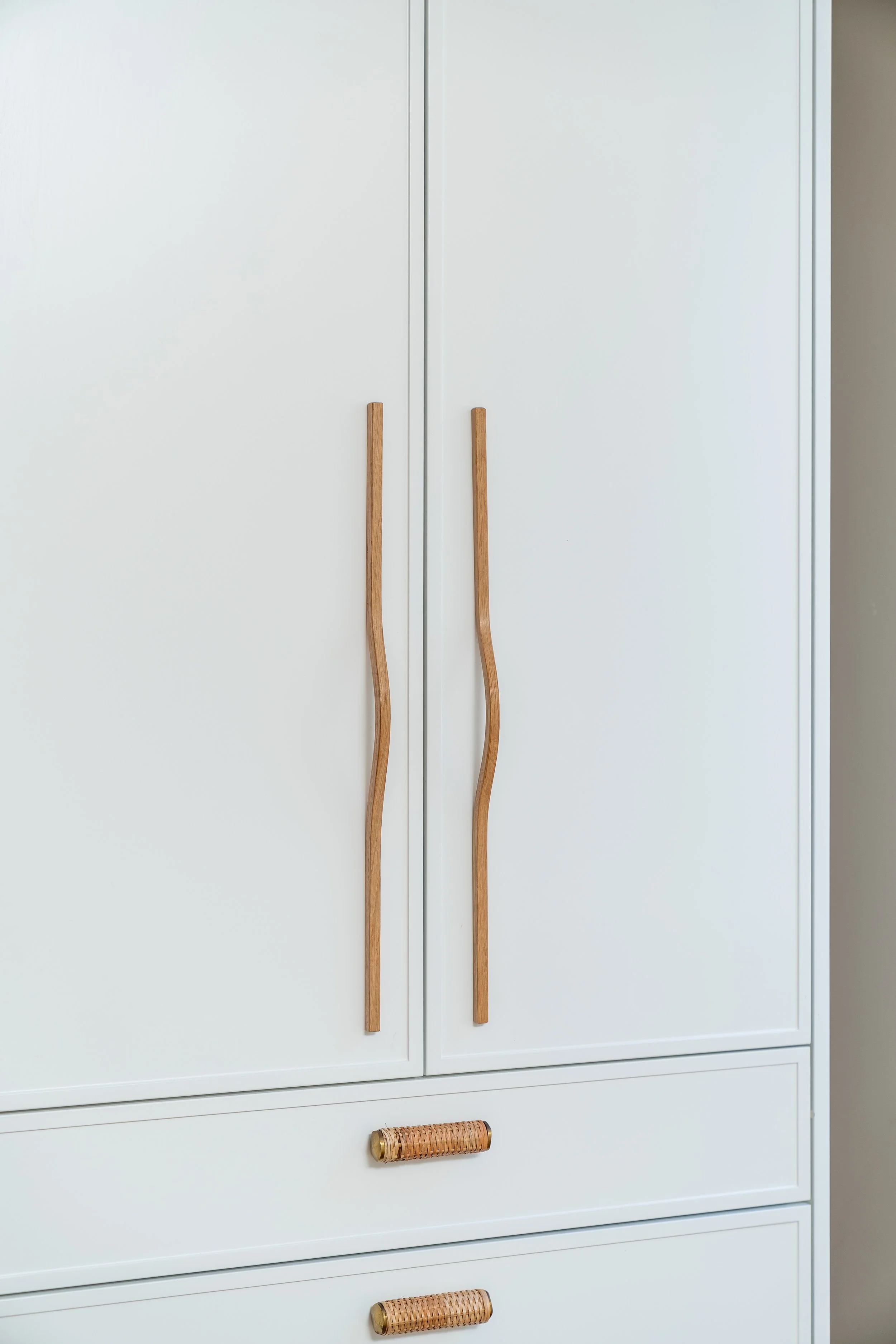 A white wardrobe with two wooden handles on the door and two woven rattan handles on the drawers.