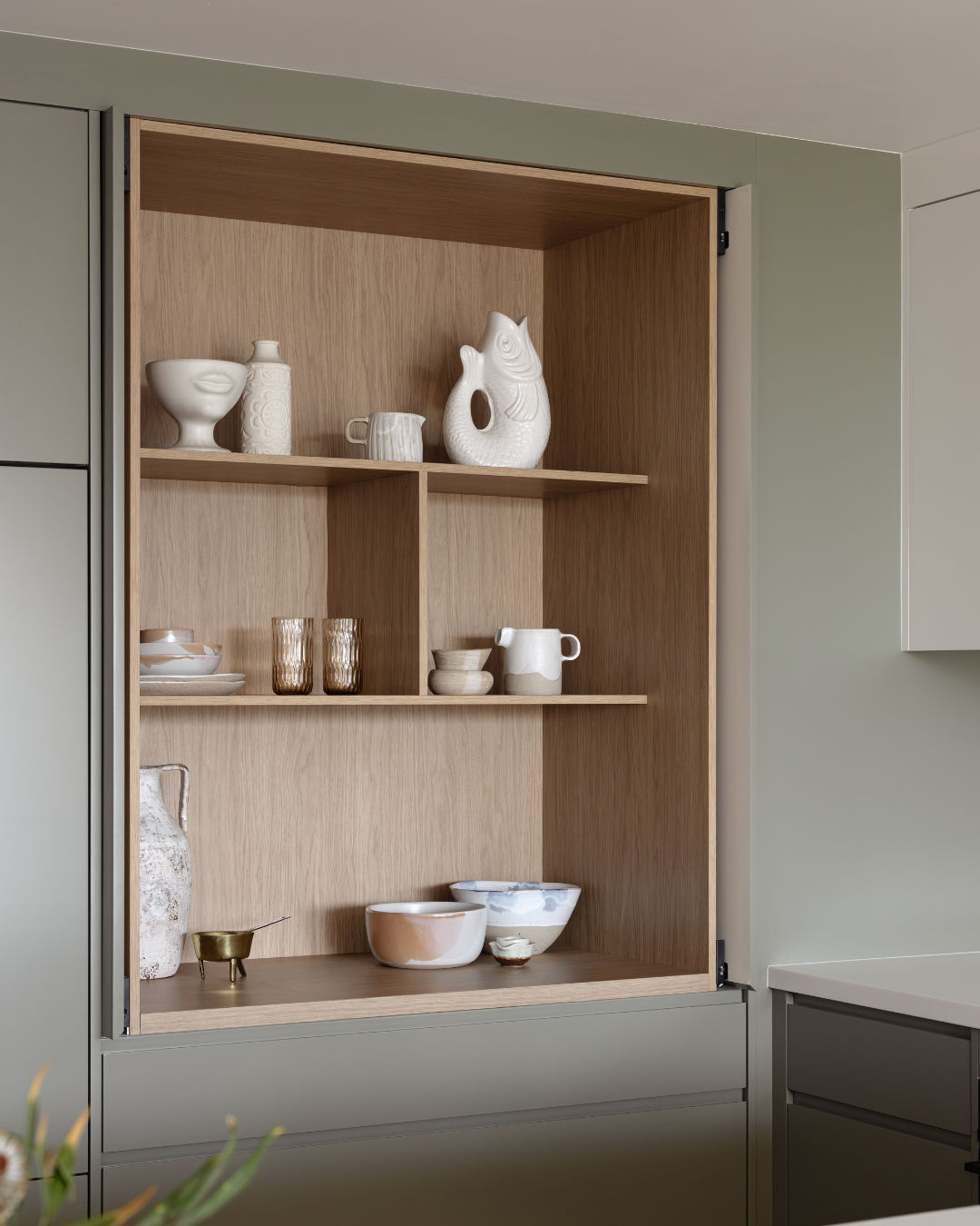 Open wooden cabinet with ceramic dishes and glassware inside, in a modern kitchen.