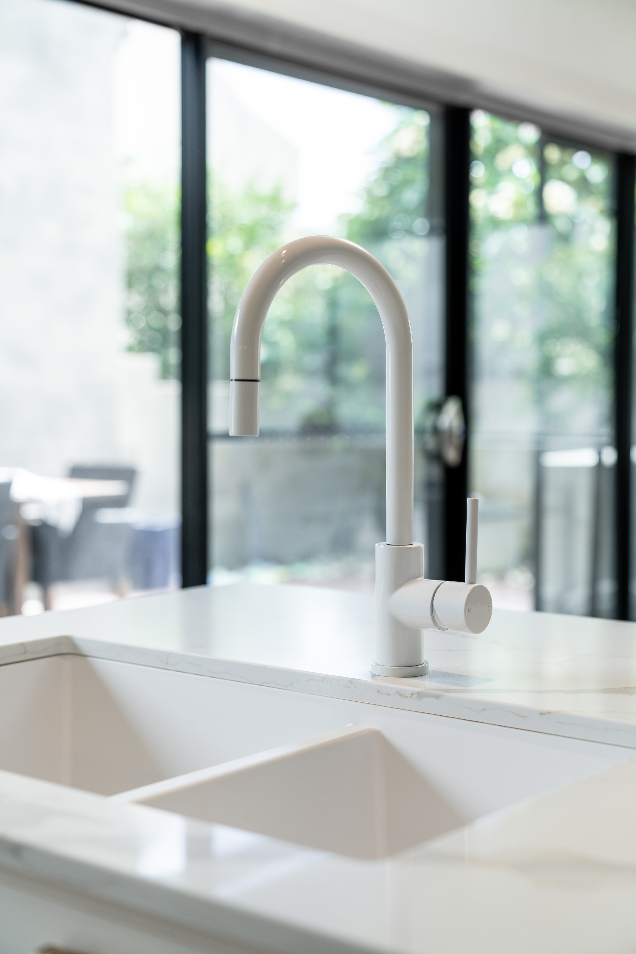 Modern kitchen sink with a white curved faucet and a large window in the background showing greenery.