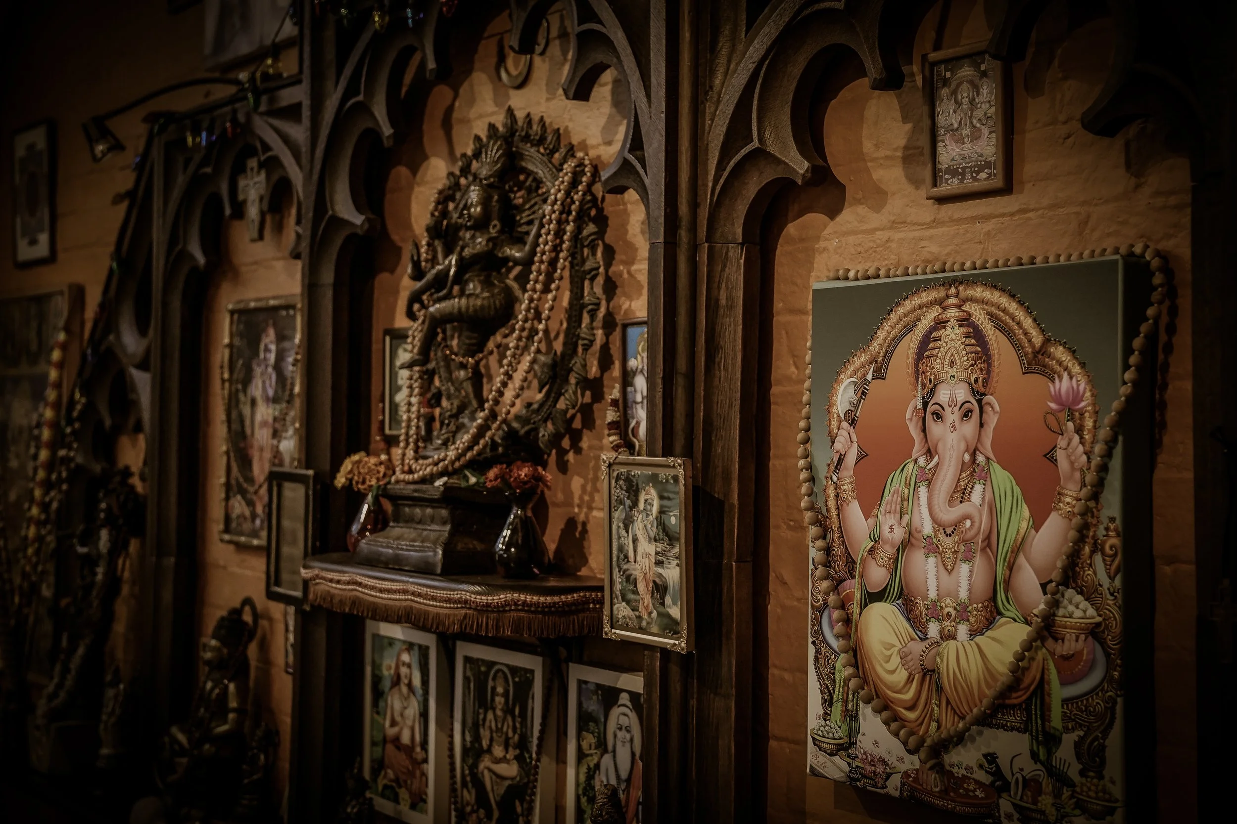 Wall decorated with religious images and sculptures, including a prominent picture of Lord Ganesha, surrounded by other framed art and religious artifacts.