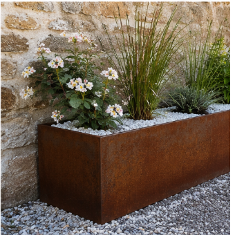 Un jardinière en acier corten avec des plantes vertes et des fleurs blanches, placée devant un mur en pierre.