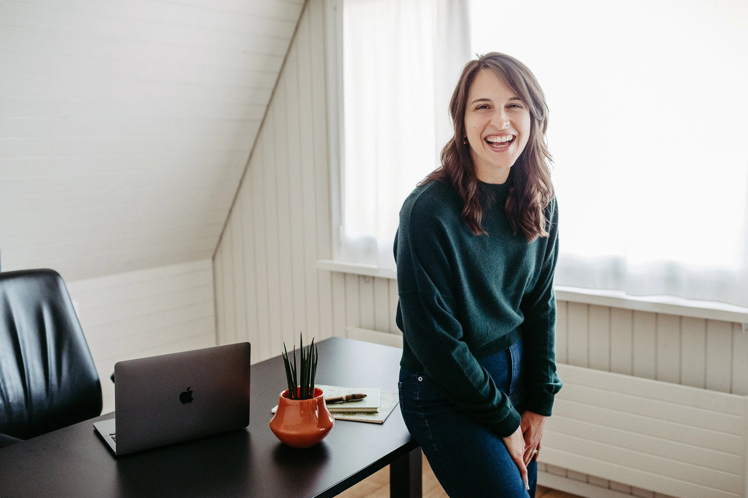 Kara leaning against her desk and laughing while looking at the camera