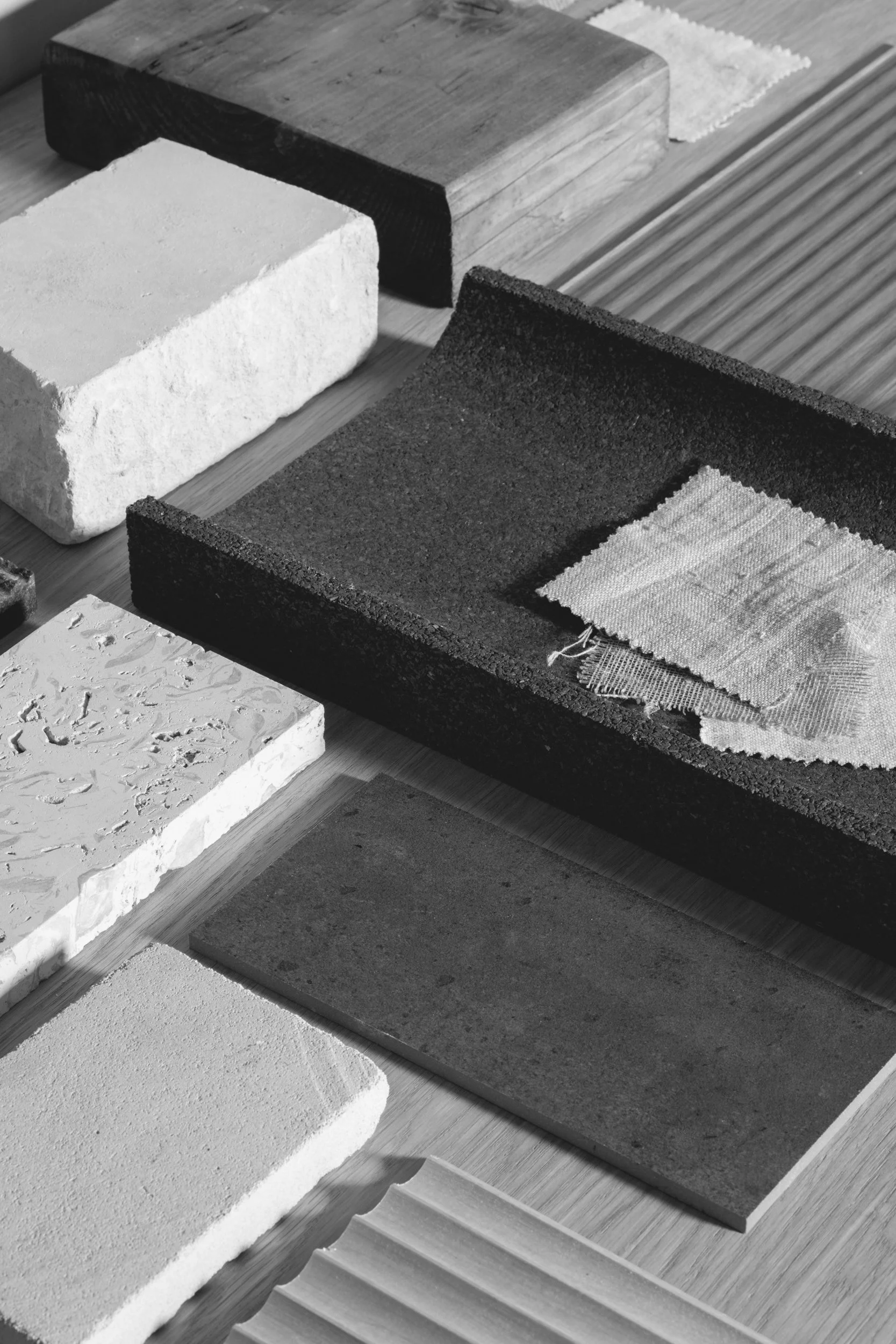 Black and white photo of different textured wall samples, including bricks, panels, and tiles, arranged on a wooden surface for selection or comparison.