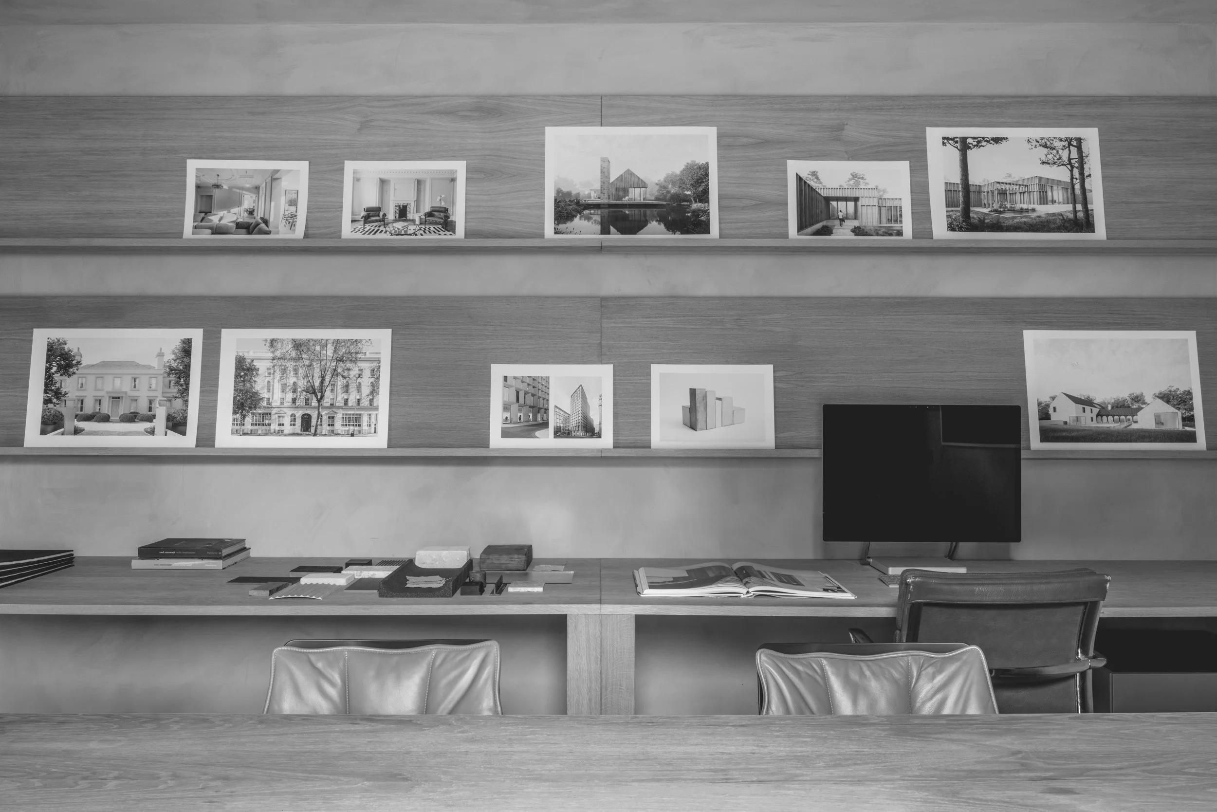Photographs of architectural designs and buildings, spread across a wooden desk with books, samples, and a computer monitor.