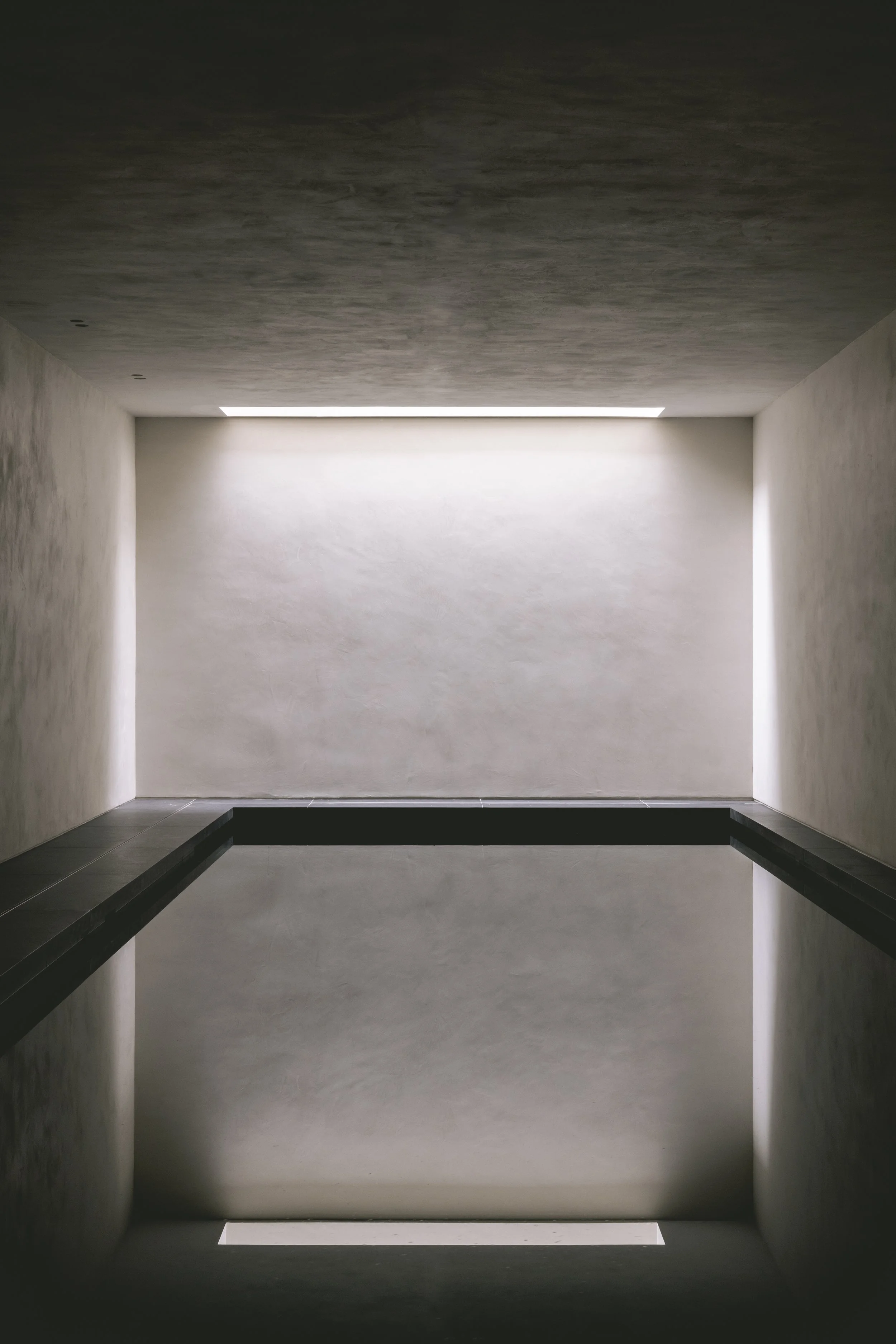 Minimalist interior with a white wall, dark handrails, and a narrow horizontal window near the ceiling allowing natural light.