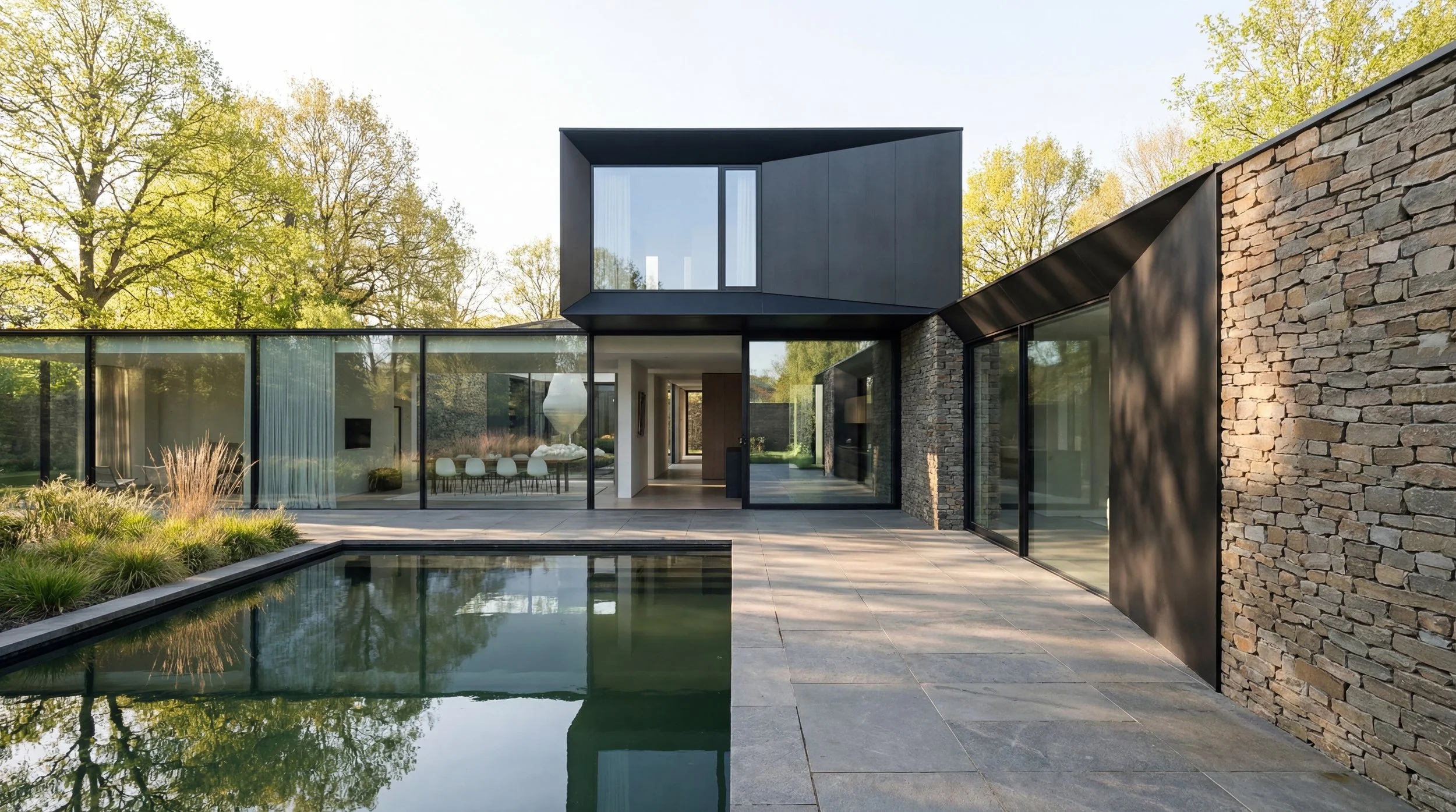Modern house with large glass windows, a stone wall, and a small swimming pool, surrounded by trees and greenery.