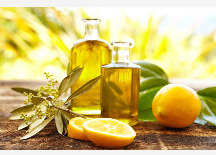 Two bottles of lemon-infused oil and fresh lemons on a rustic wooden surface.