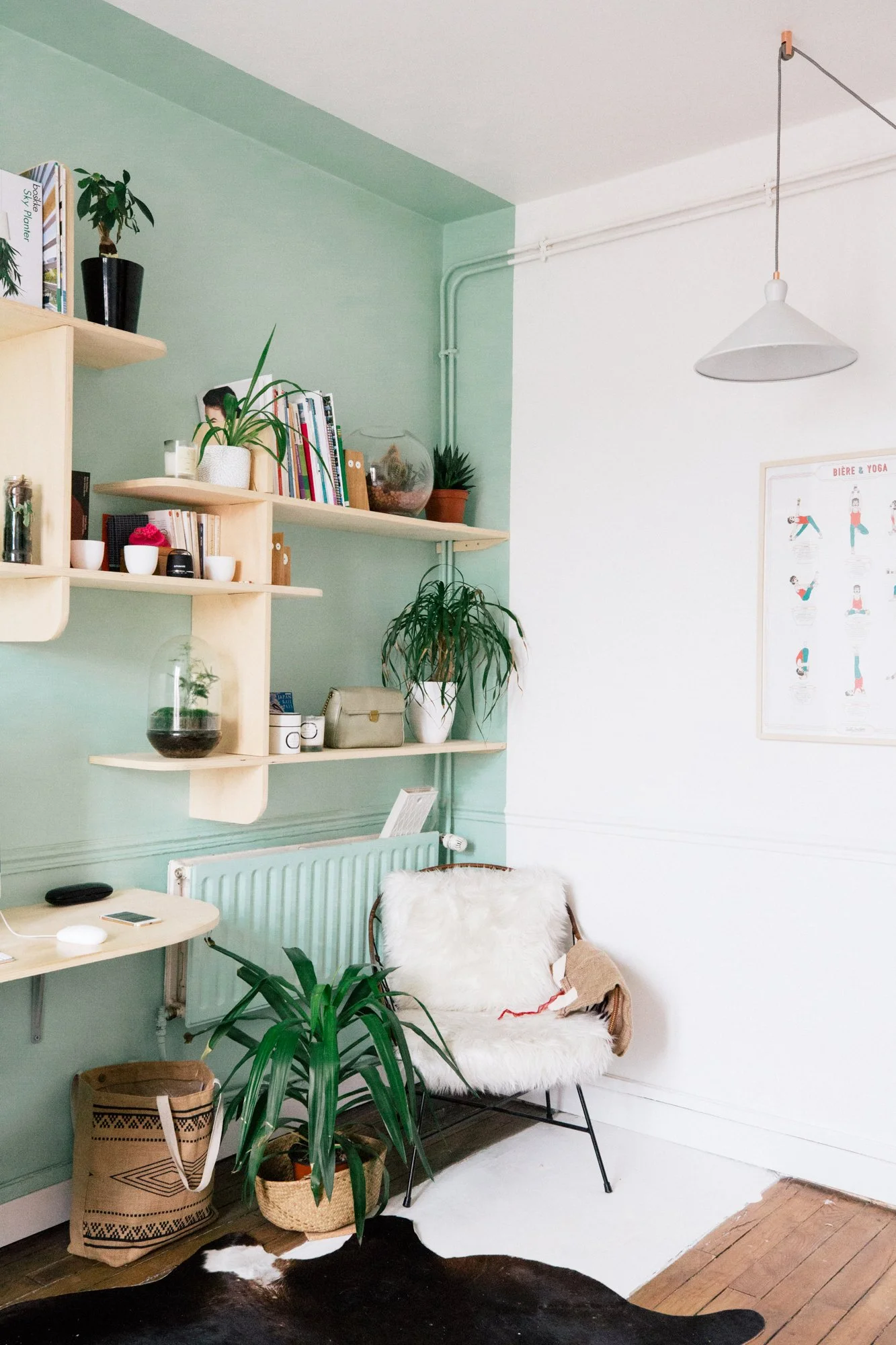 Un coin salon avec un fauteuil avec une housse en fourrure, des plantes vertes, une étagère en bois, un tableau d'instructions de yoga, et un tapis en peau de vache sur un sol en bois.