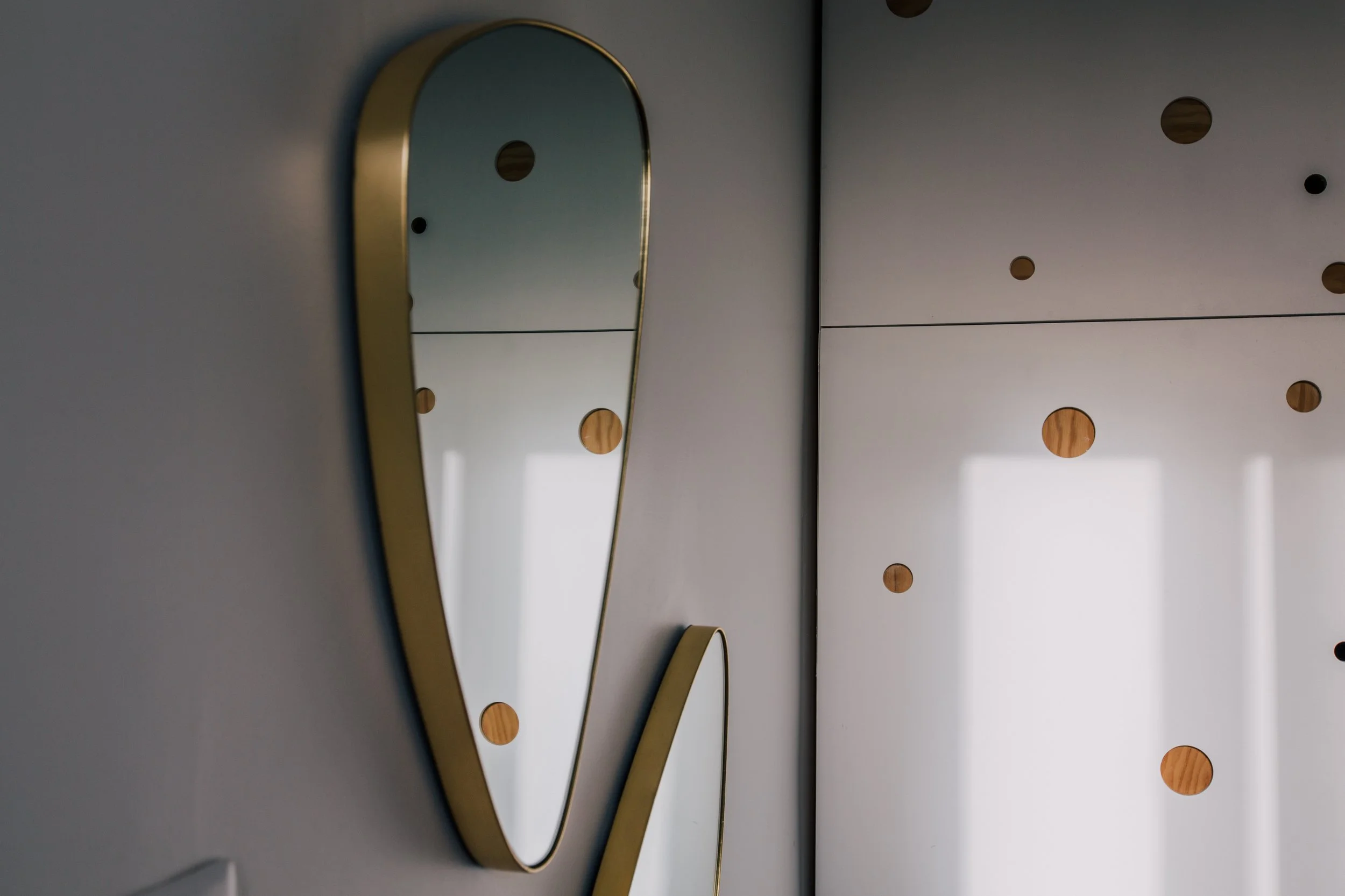 Un miroir oval avec cadre doré fixé sur un mur blanc, reflet dans le miroir.