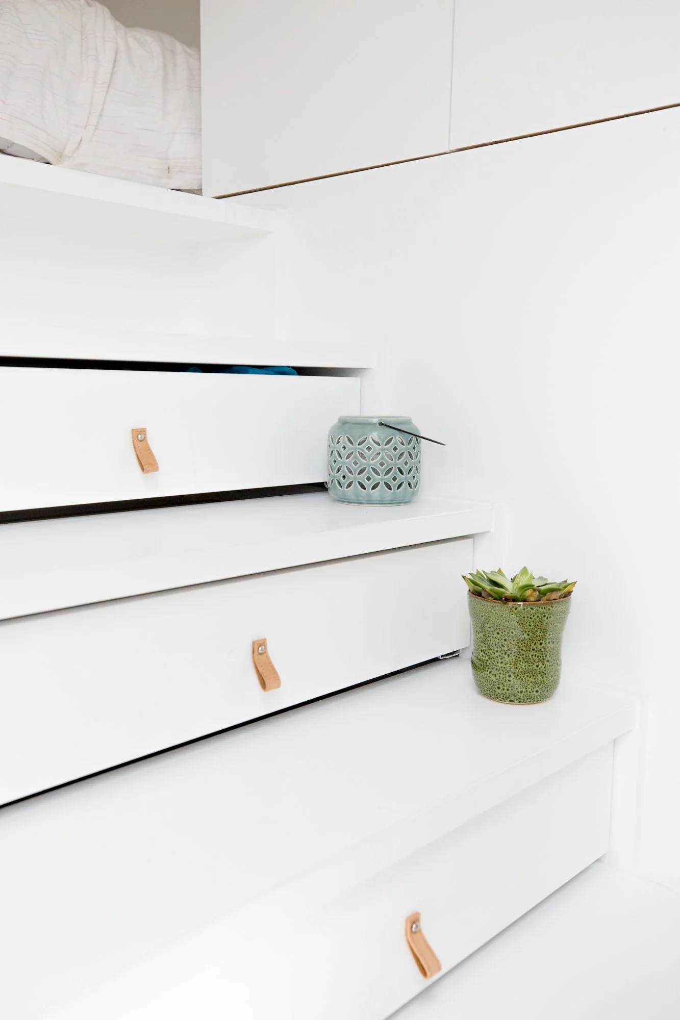 Étagère blanche avec deux pots, un en céramique avec des motifs circulaires et un autre en terre cuite avec des succulentes, dans un environnement minimaliste.