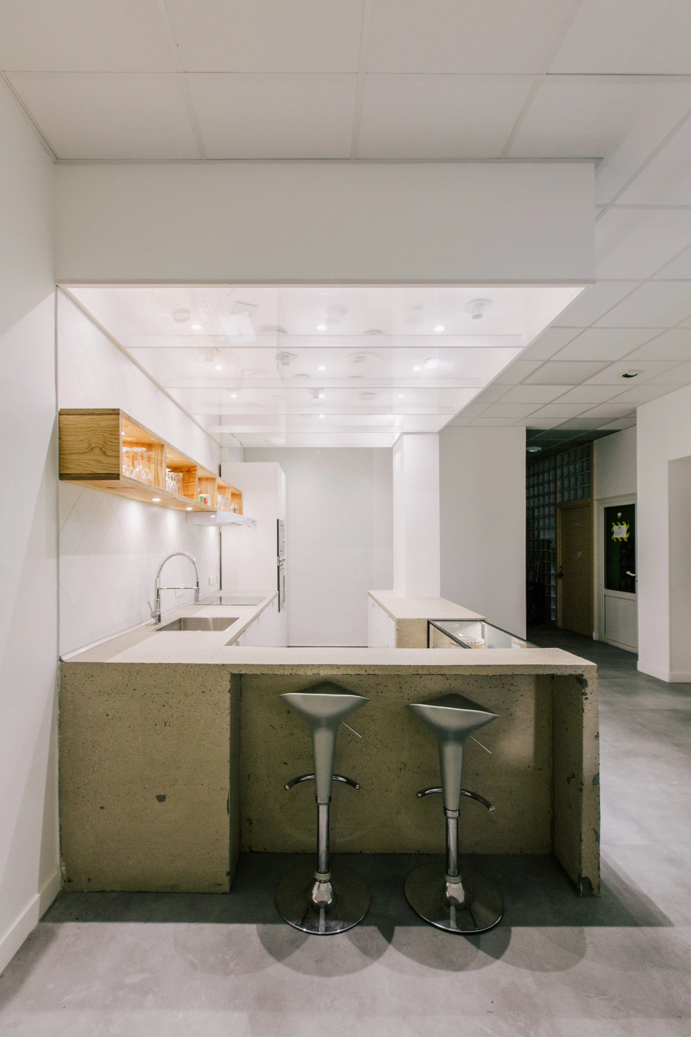 Bar en béton avec deux tabourets en acier inoxydable, dans une cuisine moderne blanche