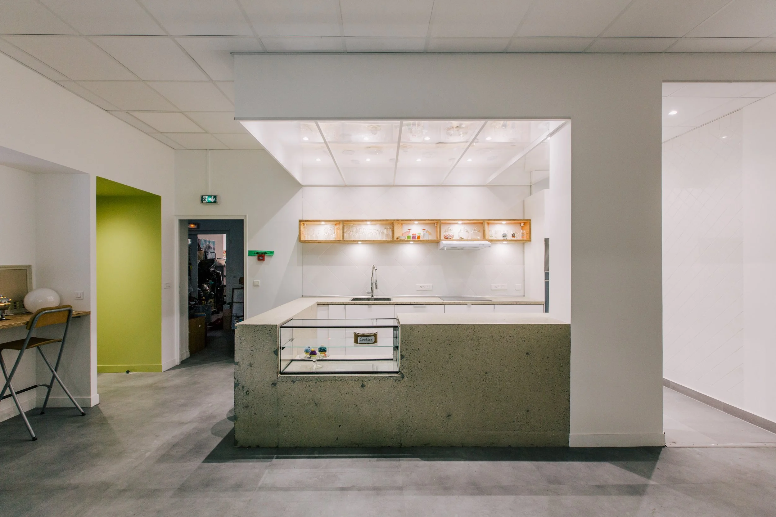 Intérieur d'une cuisine moderne avec un comptoir en granit, un évier, une étagère en bois éclairée, un mur blanc et un plafond suspendu.