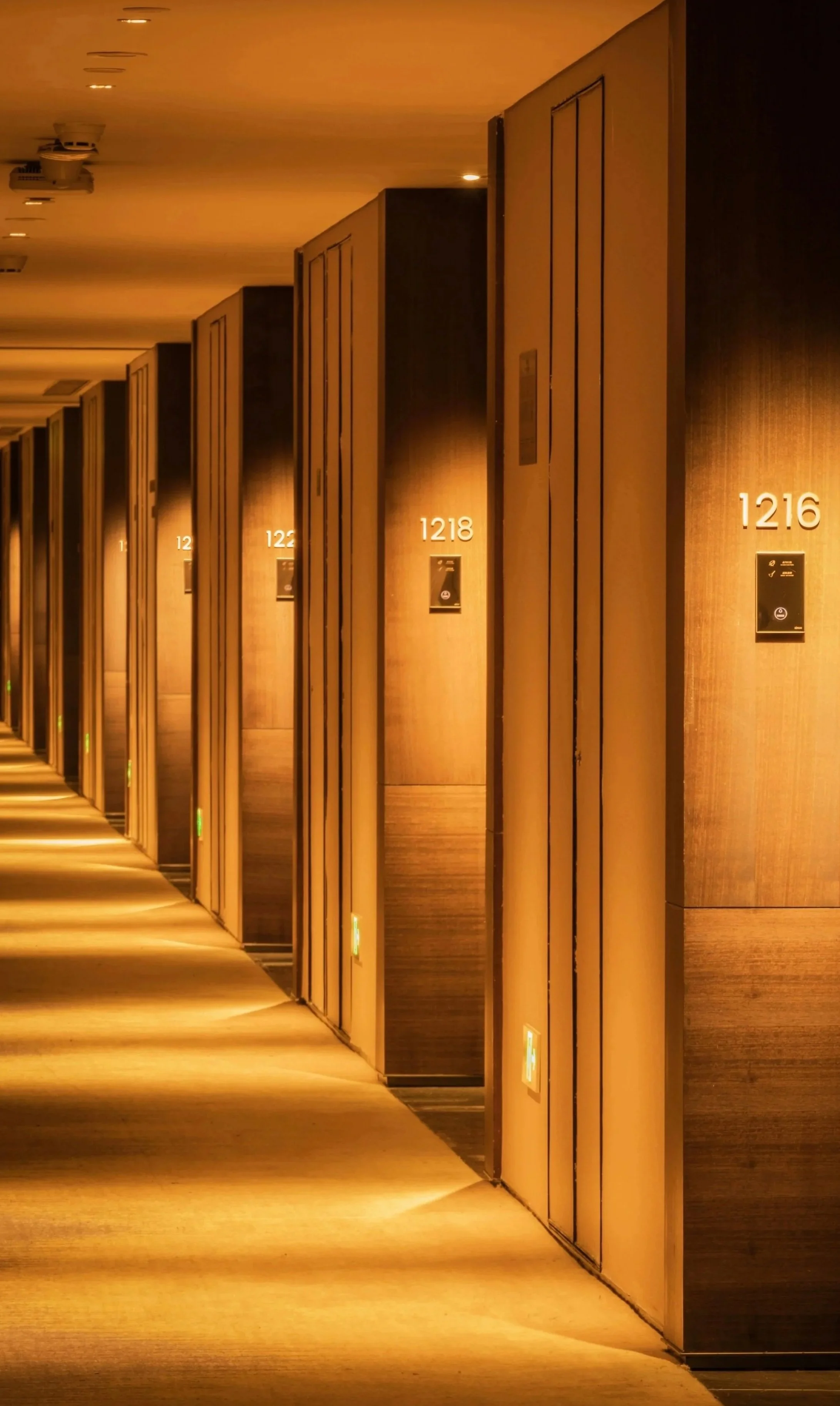 Un couloir d'hôtel avec des portes d'ascenseur en bois, numérotées 1216 à 1220, éclairé par un éclairage tamisé