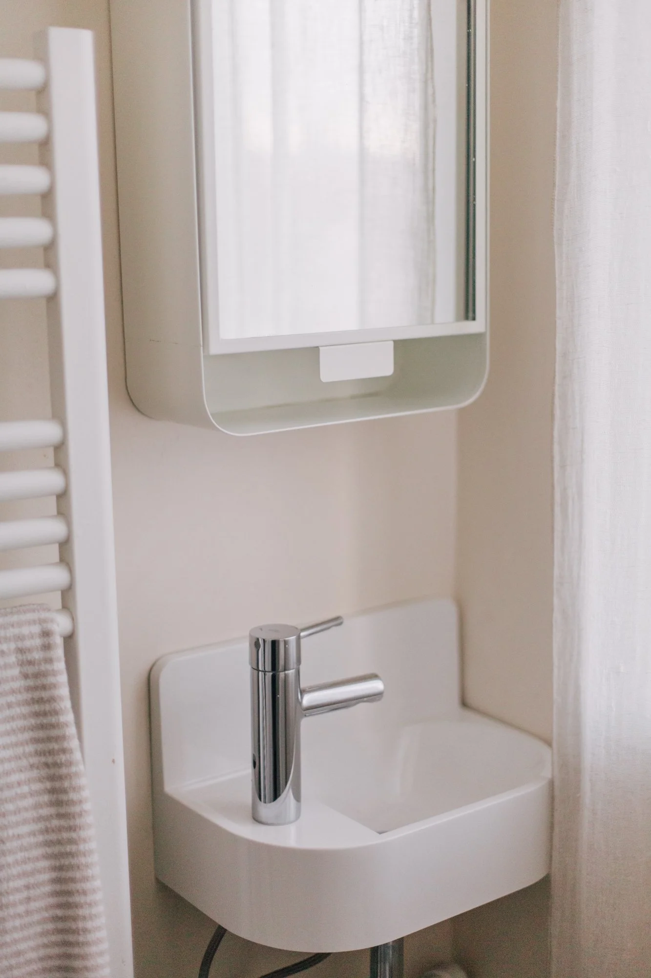 Un miroir, un lavabo blanc avec un robinet en chrome, et un petit meuble dans une salle de bain.