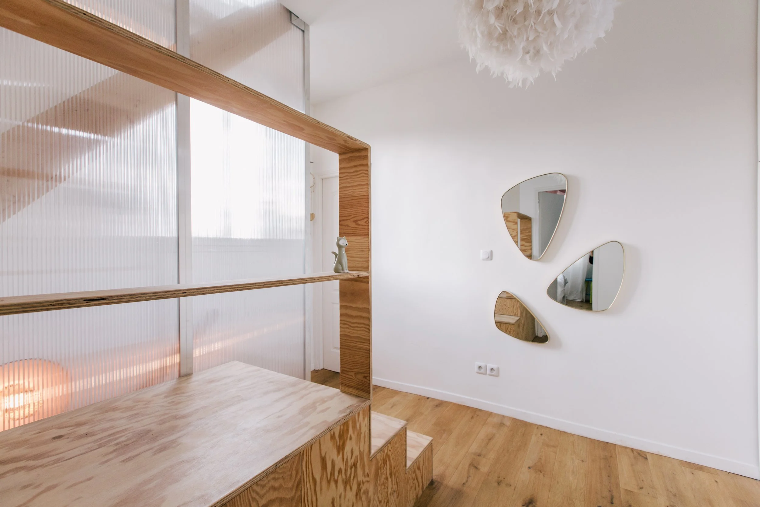 Intérieur d'une pièce avec murs blancs, miroir décoratif murale, étagère en bois et parquet en bois clair.