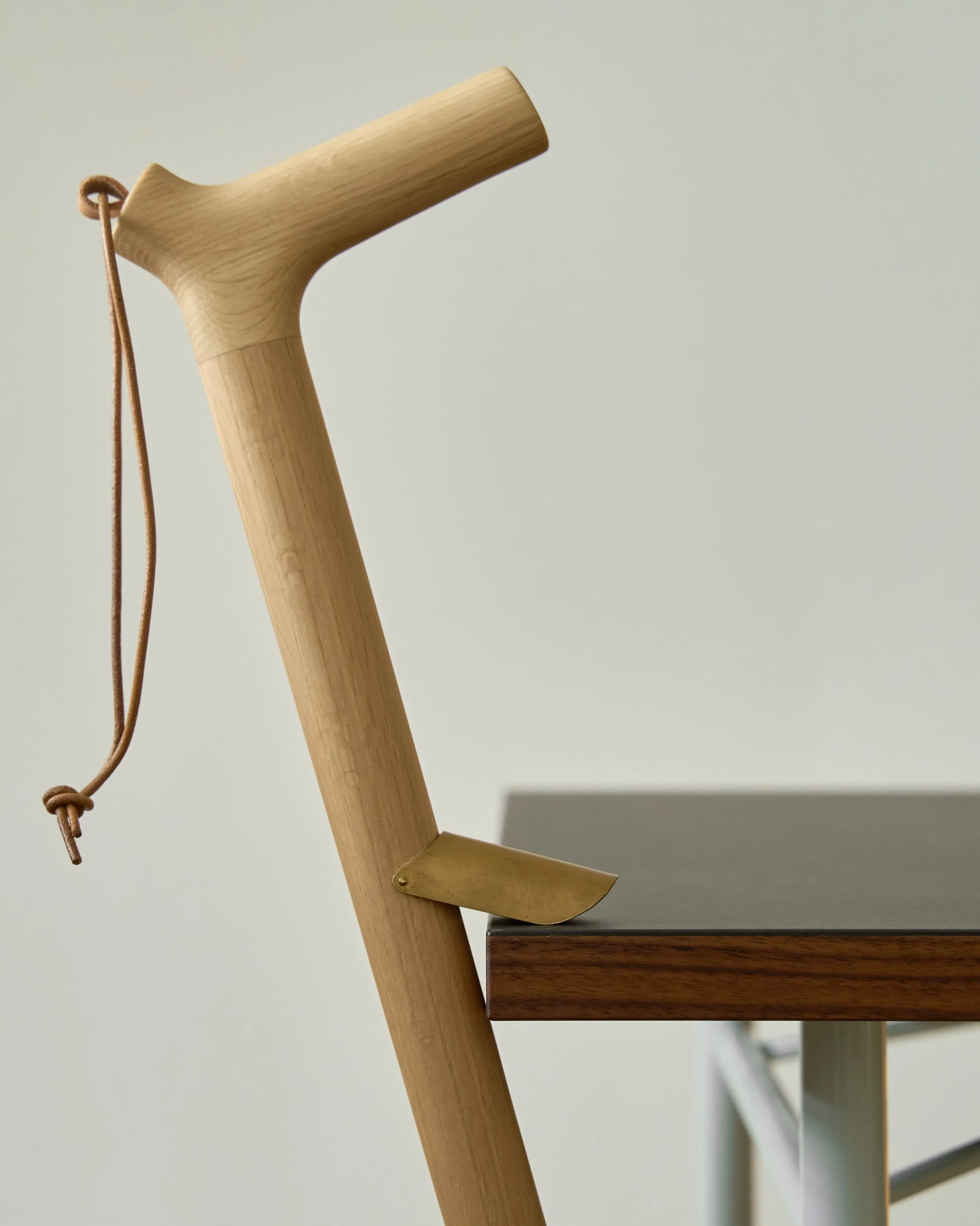 Close-up of a wooden staircase handrail with a leather strap hanging from a corner, against a plain white wall.