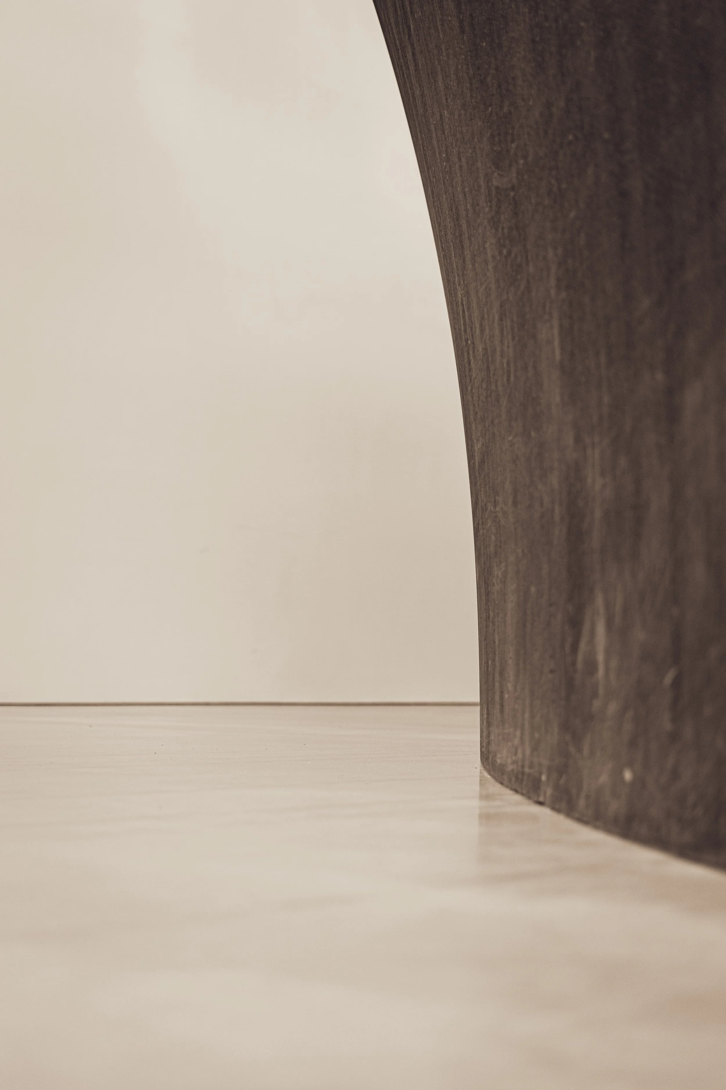 Close-up of a wooden table's curved edge with a light-colored background and a light wood floor.
