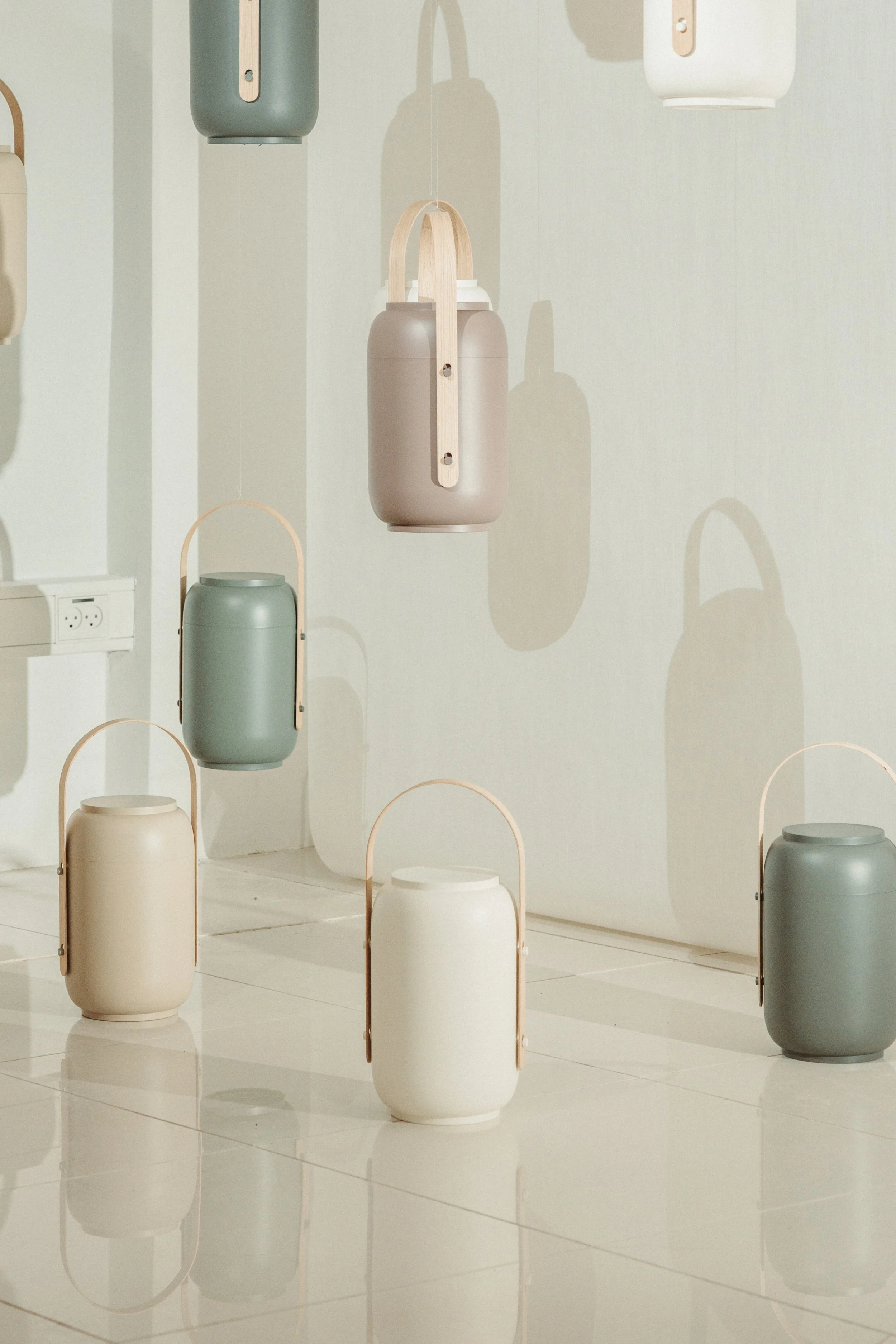 Colorful modern hanging lamps and decorative vases displayed on a white wall and floor, creating a minimalist aesthetic.