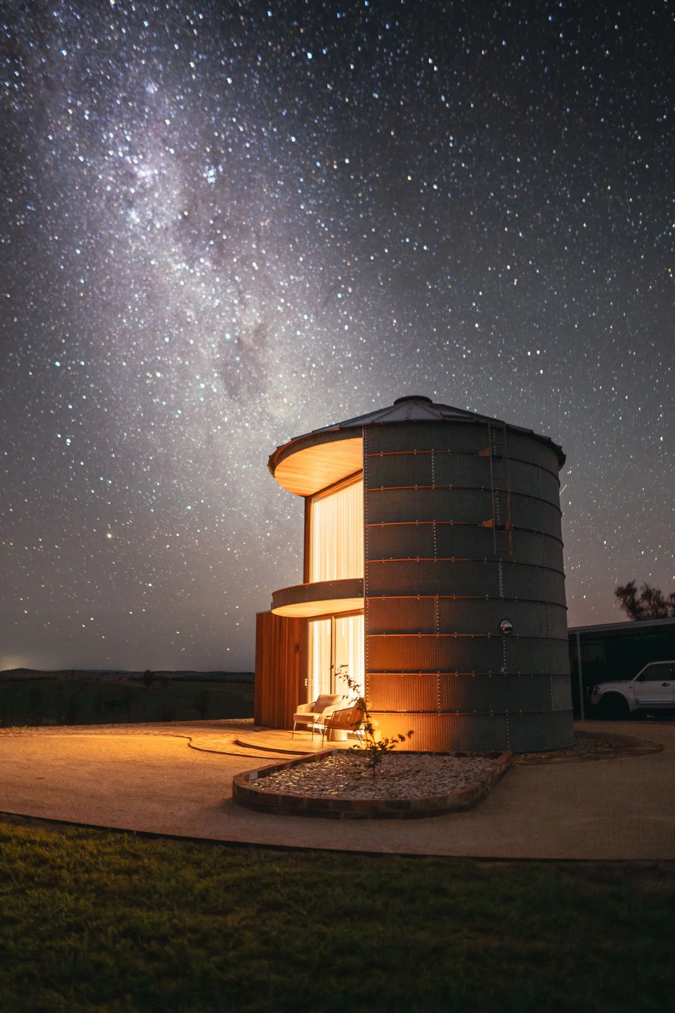 A large observatory building with an open door, illuminated from inside, standing under a starry night sky with the Milky Way galaxy visible.