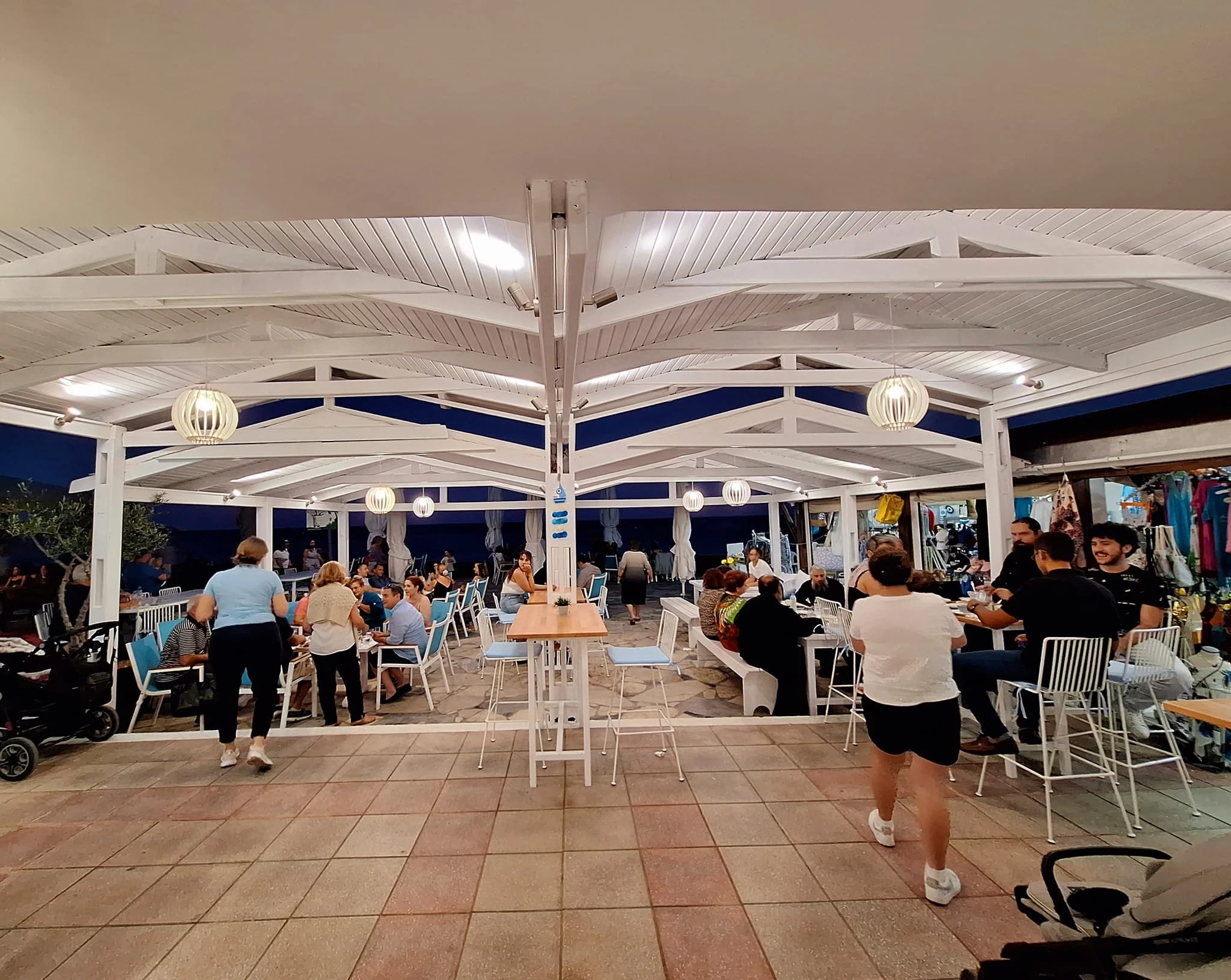 Gelateria Maria - People dining at an outdoor restaurant with white chairs and tables under a white canopy with hanging round lights during evening.