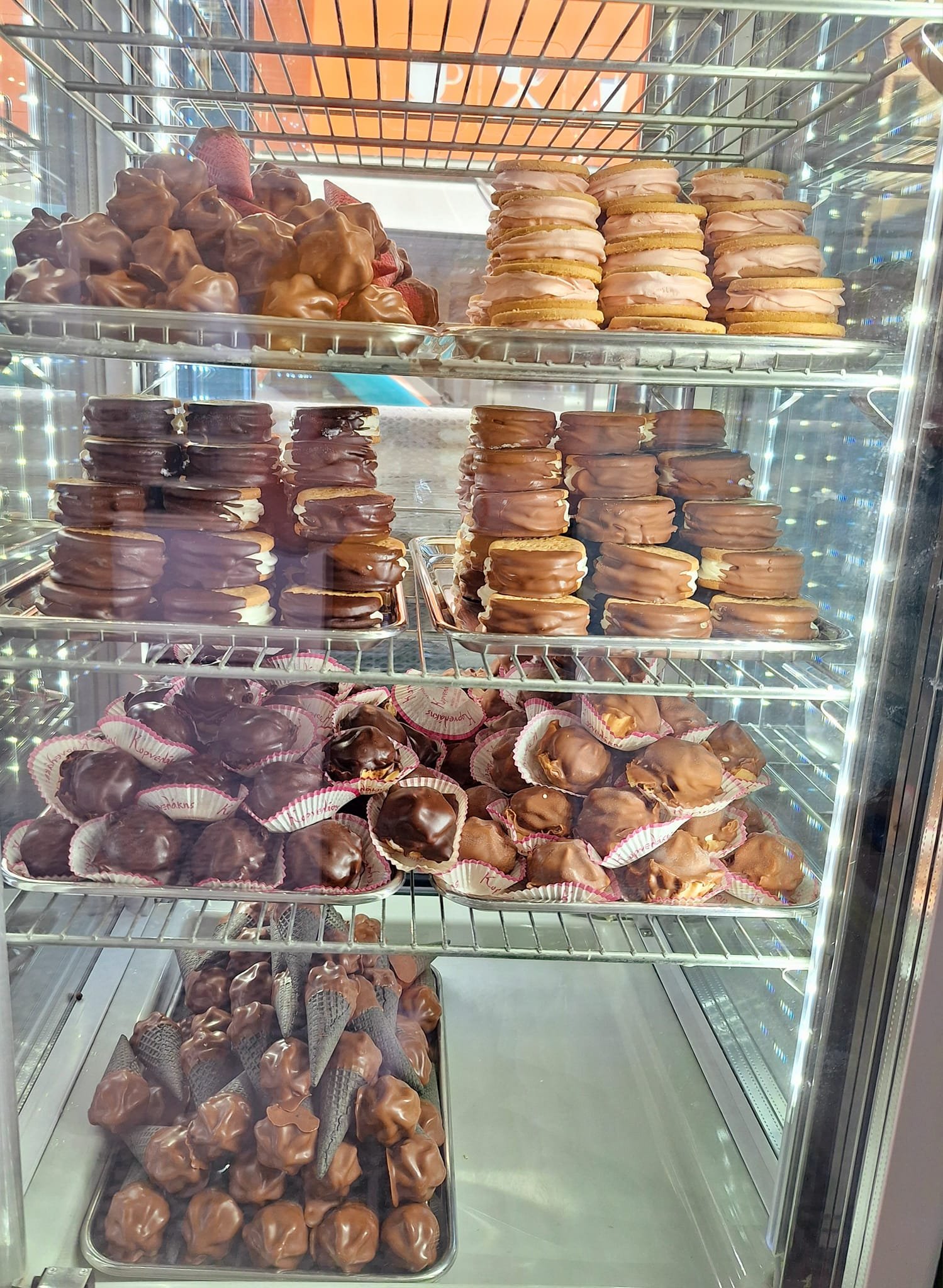Gelateria Maria - A glass display case filled with various types of chocolate-covered desserts, including chocolate-covered strawberries, eclairs, and different kinds of cookies or macarons.